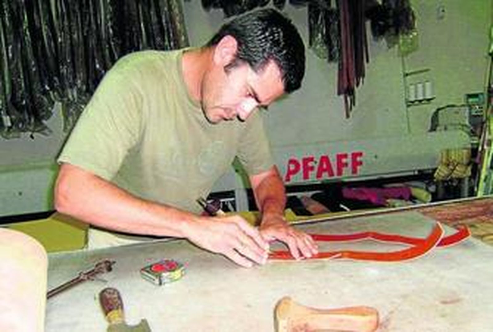 Un artesano trabaja en su taller sobre una pieza de madera, ayudado de herramientas sencillas.