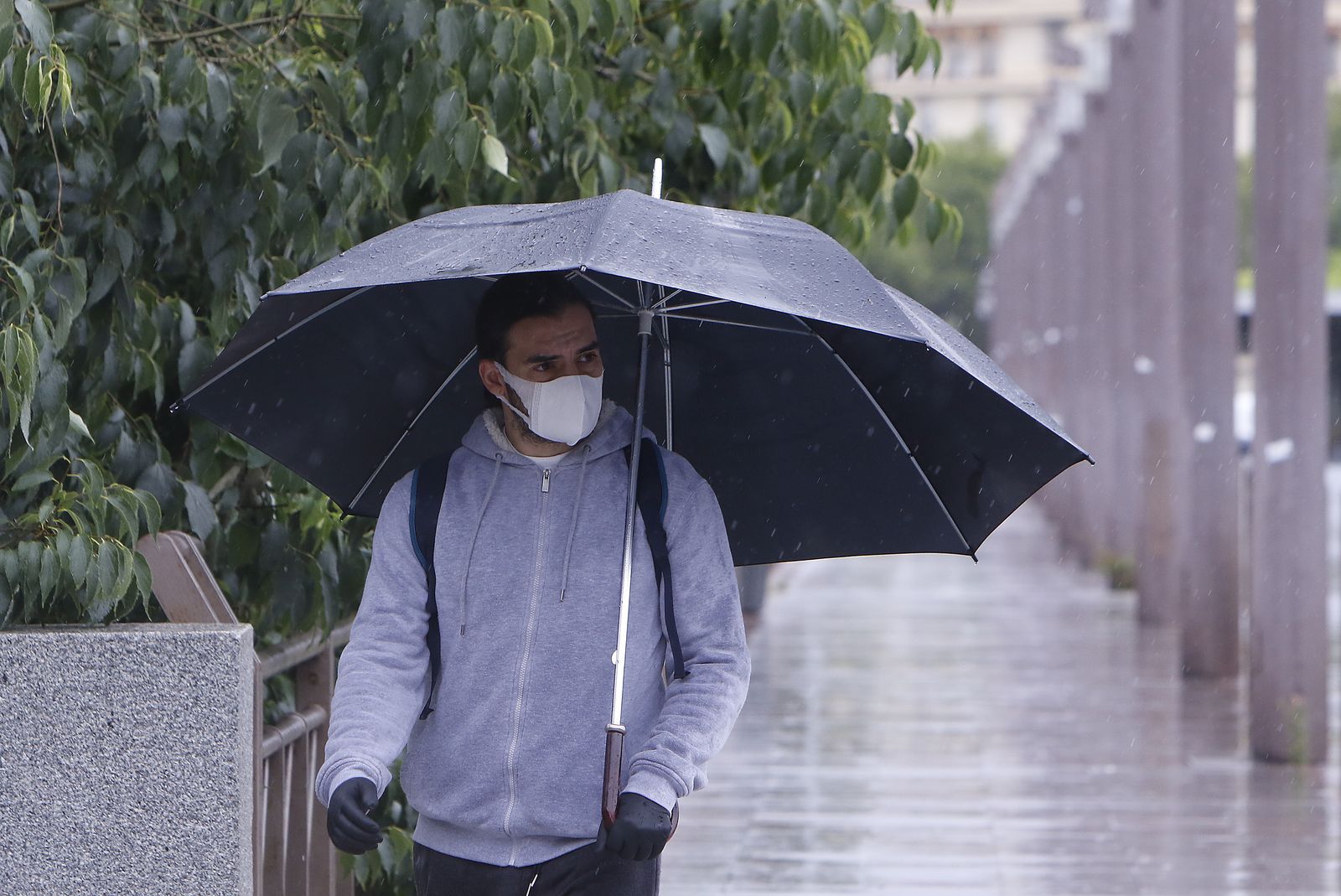 Un hombre con mascarilla se protege de la lluvia en Sevilla.