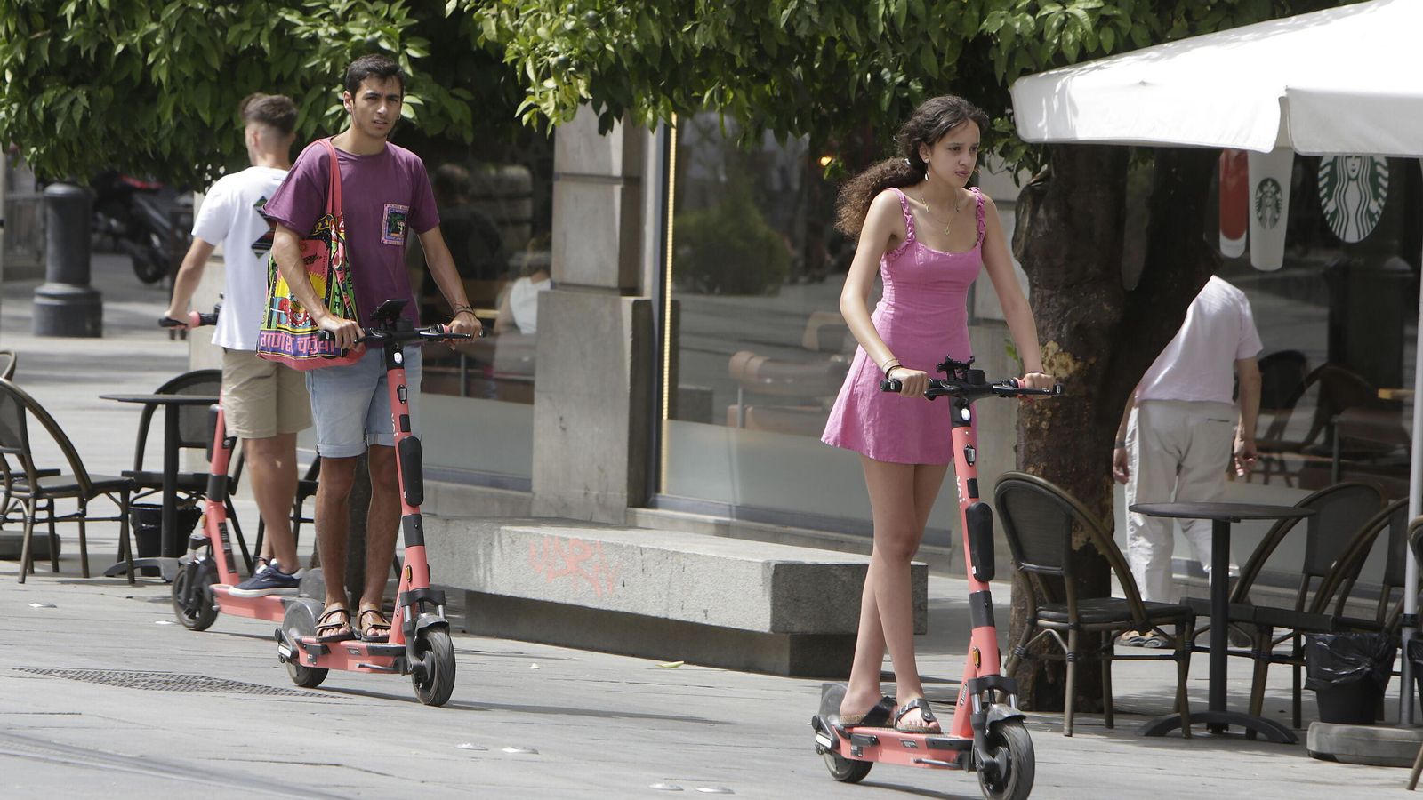 Dos usuarios en sendos patinetes de alquiler por el carril bici de la Avenida de la Constitución de Sevilla.