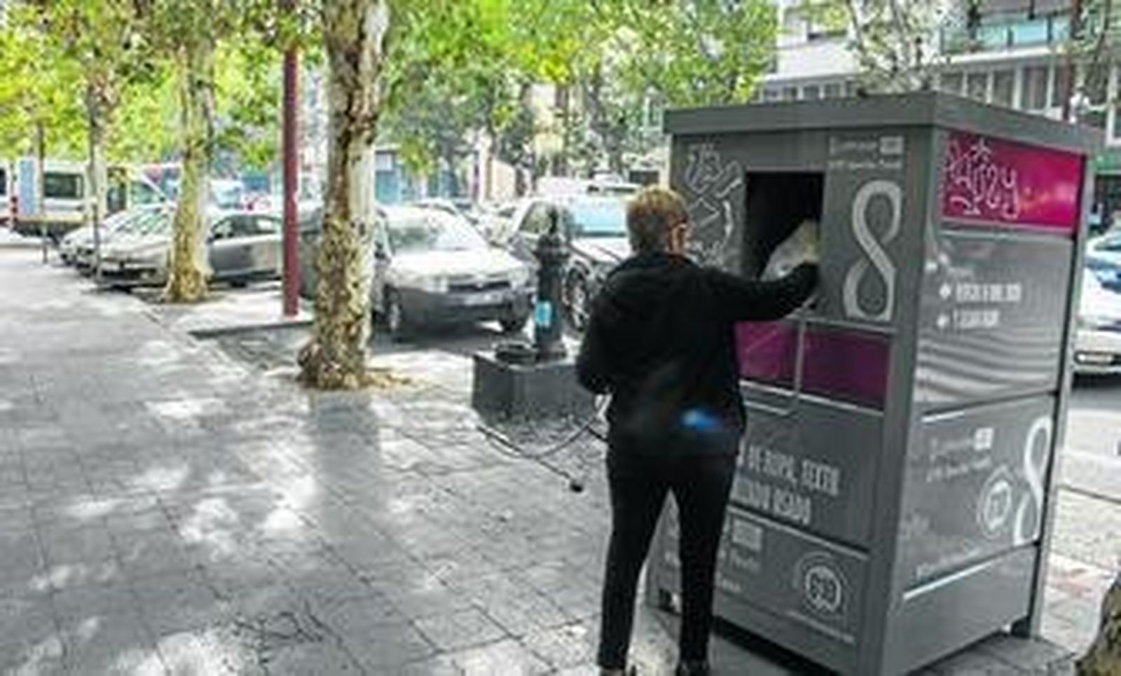 Una mujer introduce una bolsa con ropa en un contenedor de la calle Marqués de Paradas.