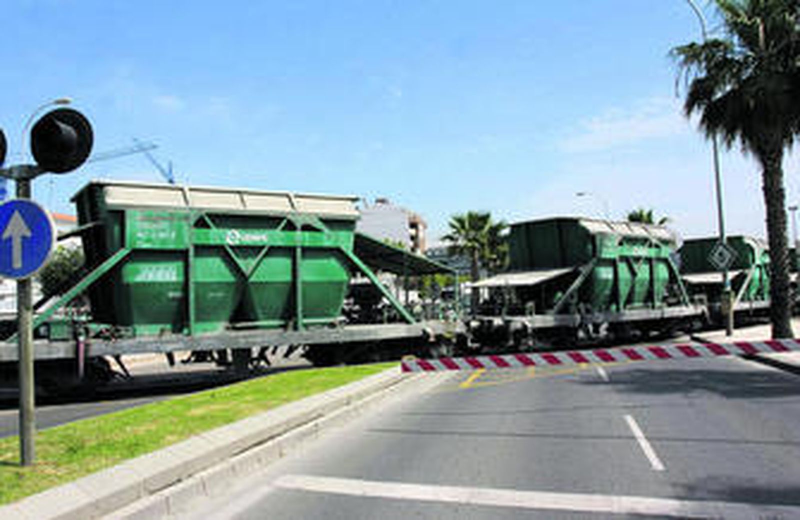 Llegada de un tren al puerto de Málaga a través de un trazado que obliga a cortar una carretera mediante barreras.