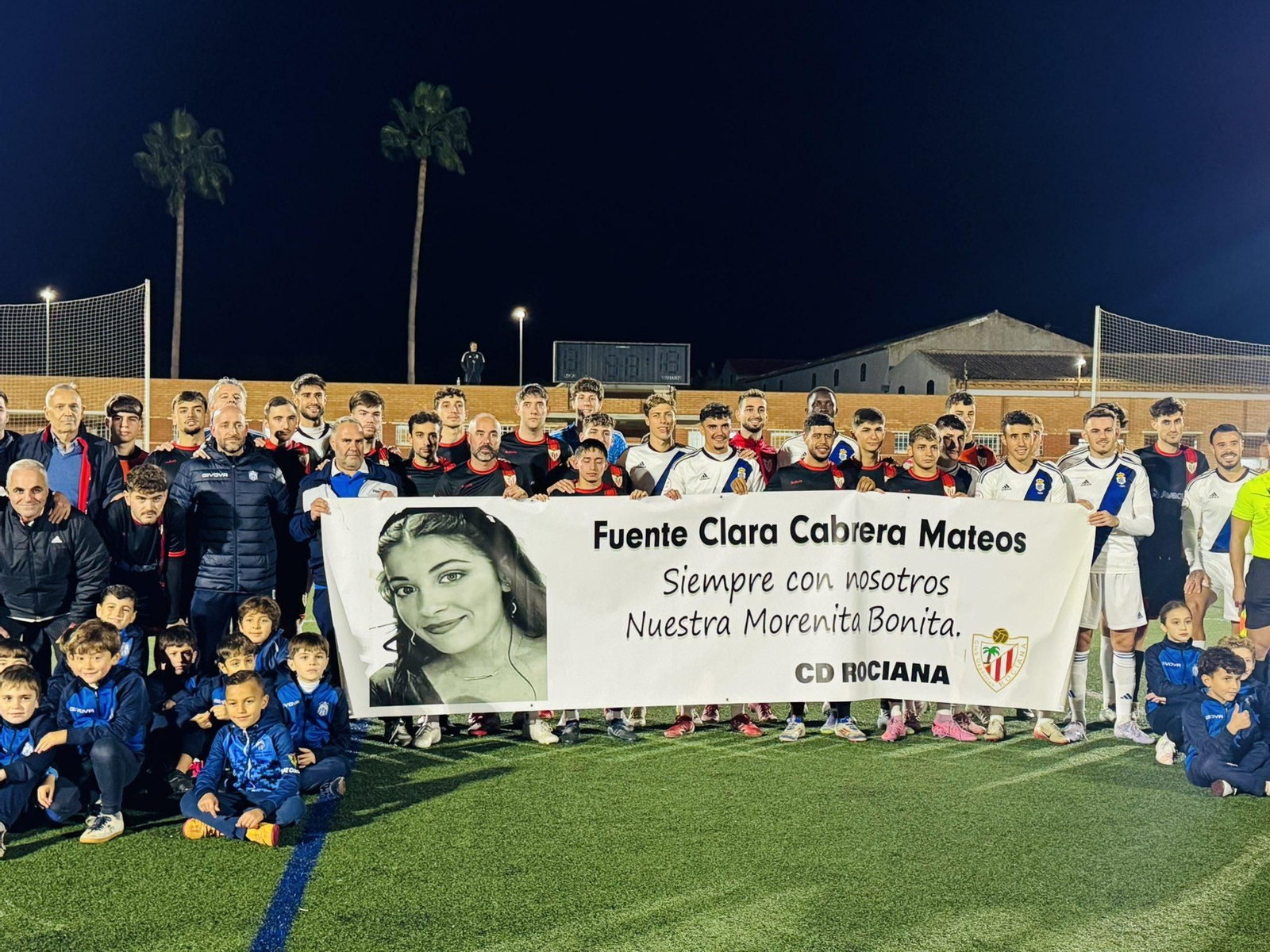 Foto de familia de los dos equipos con una pancarta en memoria de Fuente Clara Cabrera.