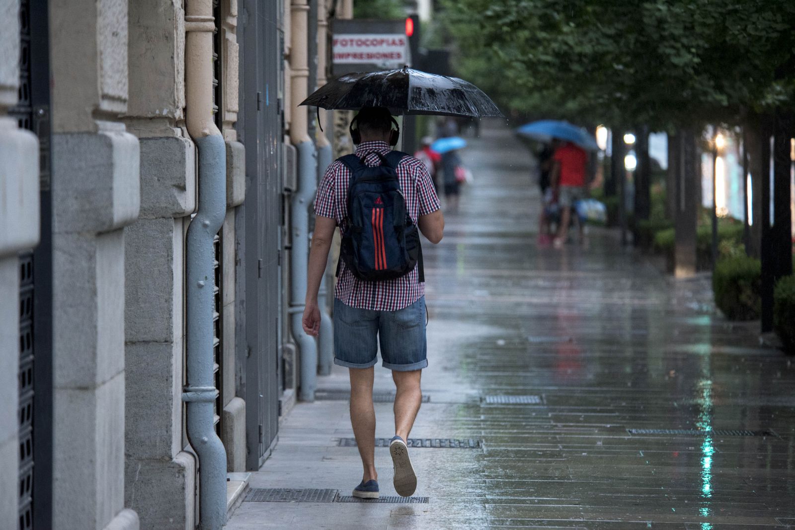 Un joven se refugia del agua en una de las pocas lluvias de este verano.