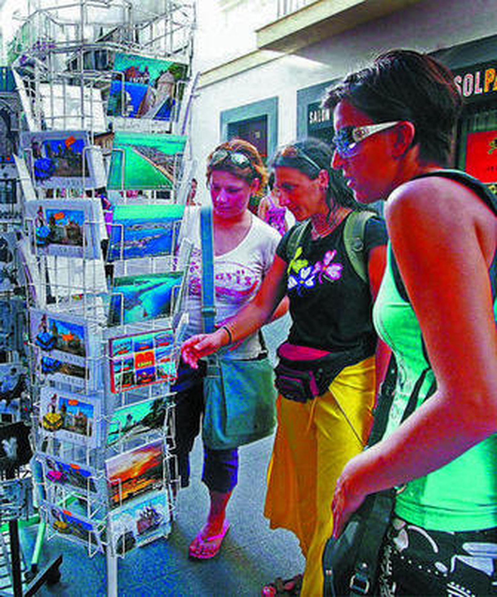 Tres turistas ojean unas postales de Cádiz en una calle del centro histórico.