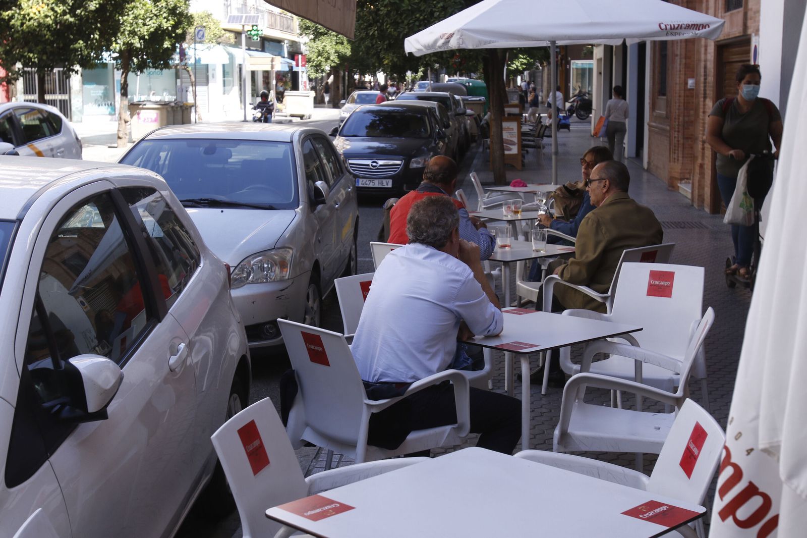 Un fila de veladores junto a varias plazas de aparcamiento.