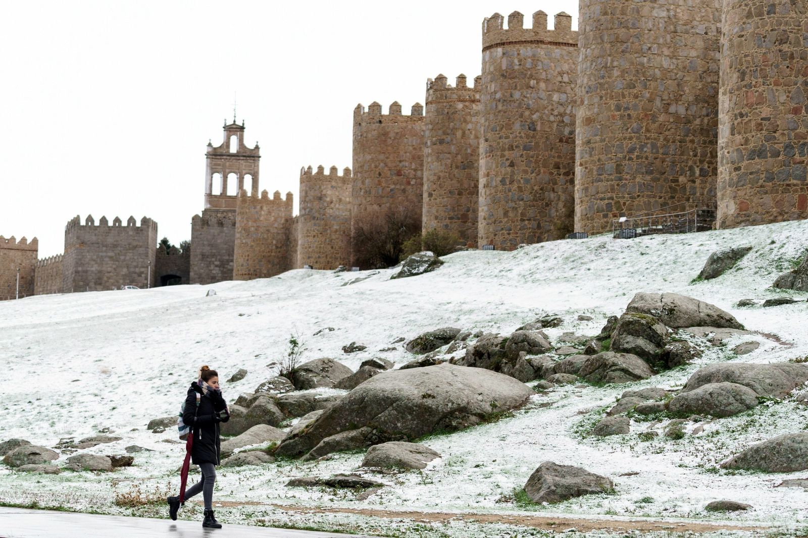 Una mujer camina junto al lienzo norte de la muralla de Ávila cubierta por una fina capa nieve.