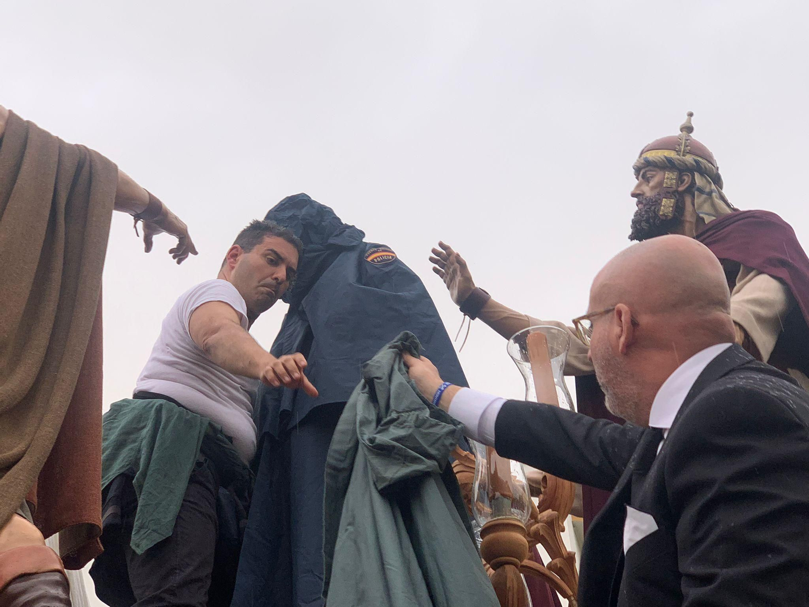 Un costalero, colocando chubasqueros a las imágenes de La Pasión.