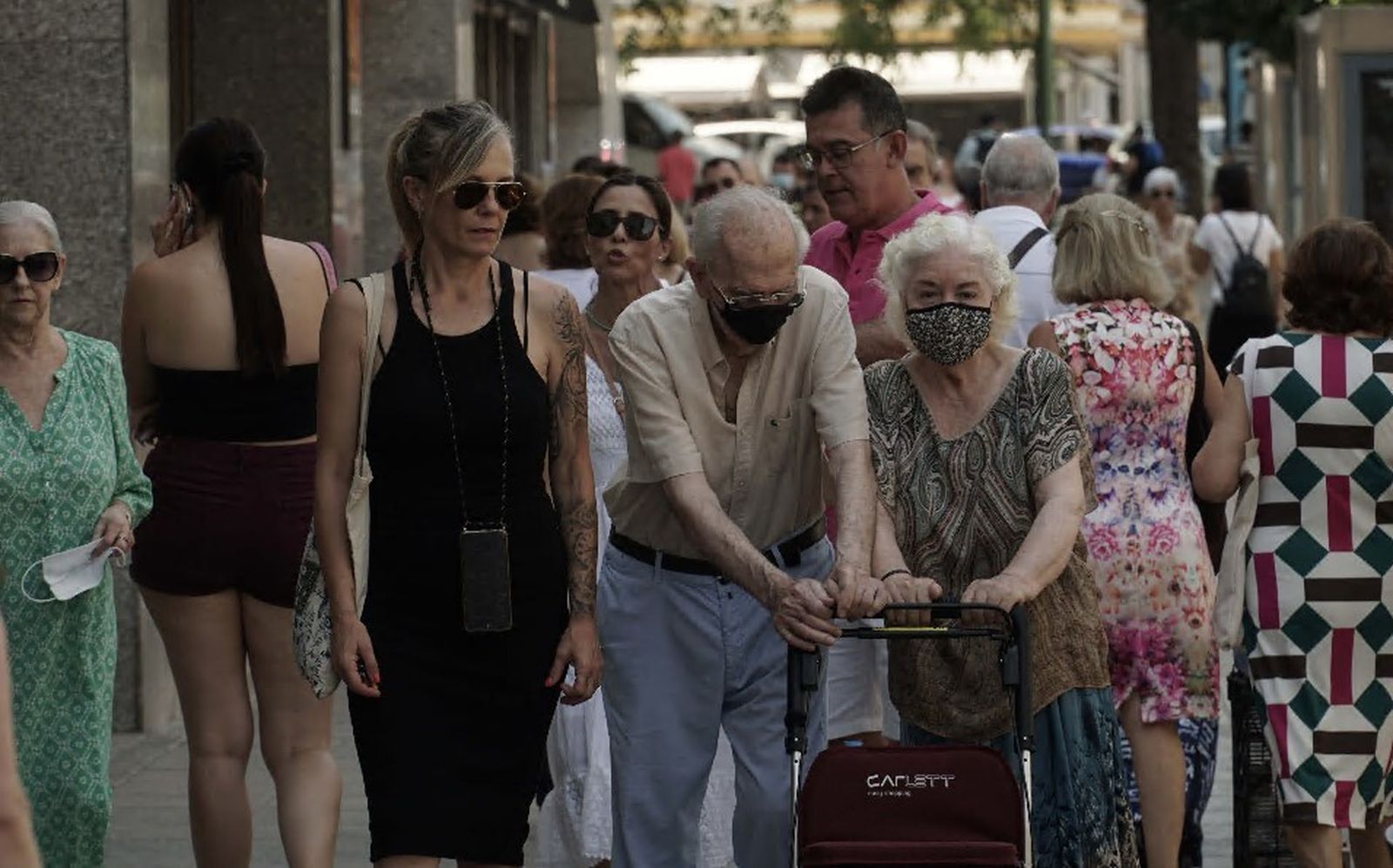 Una pareja de ancianos con mascarilla, en el centro de la imagen, entre numerosas personas sin ella por la calle.