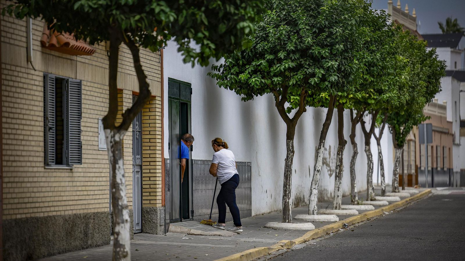 Una mujer barre la puerta de su casa.