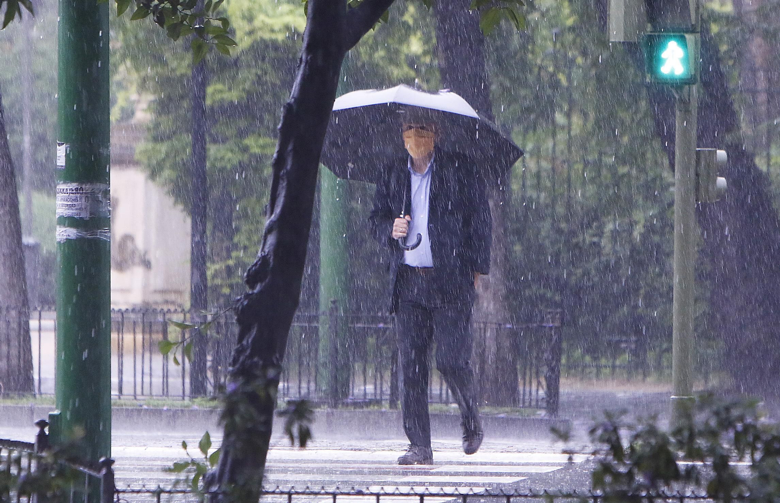 Un hombre pasea con una mascarilla y un paraguas.