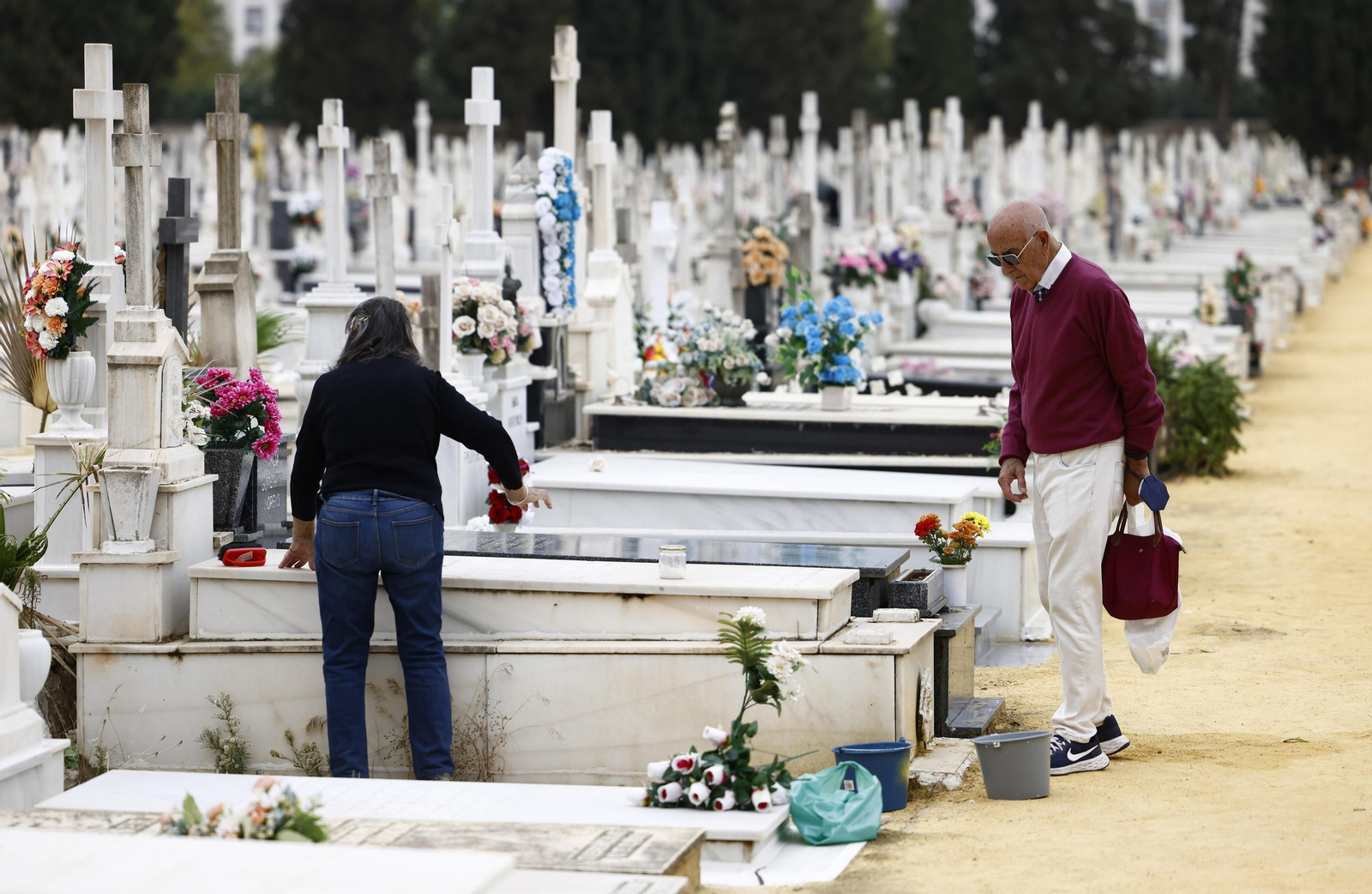 Dos personas adecentan una tumba de suelo en el cementerio de Sevilla.
