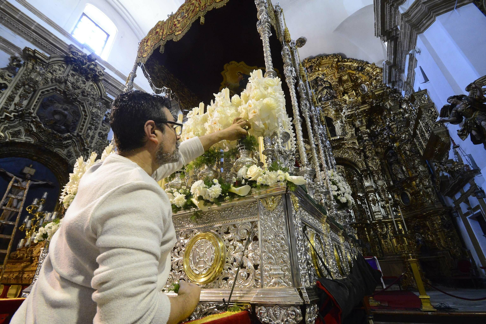 Un cofrade de Las Penas ultima el exorno floral del paso de palio de Caridad