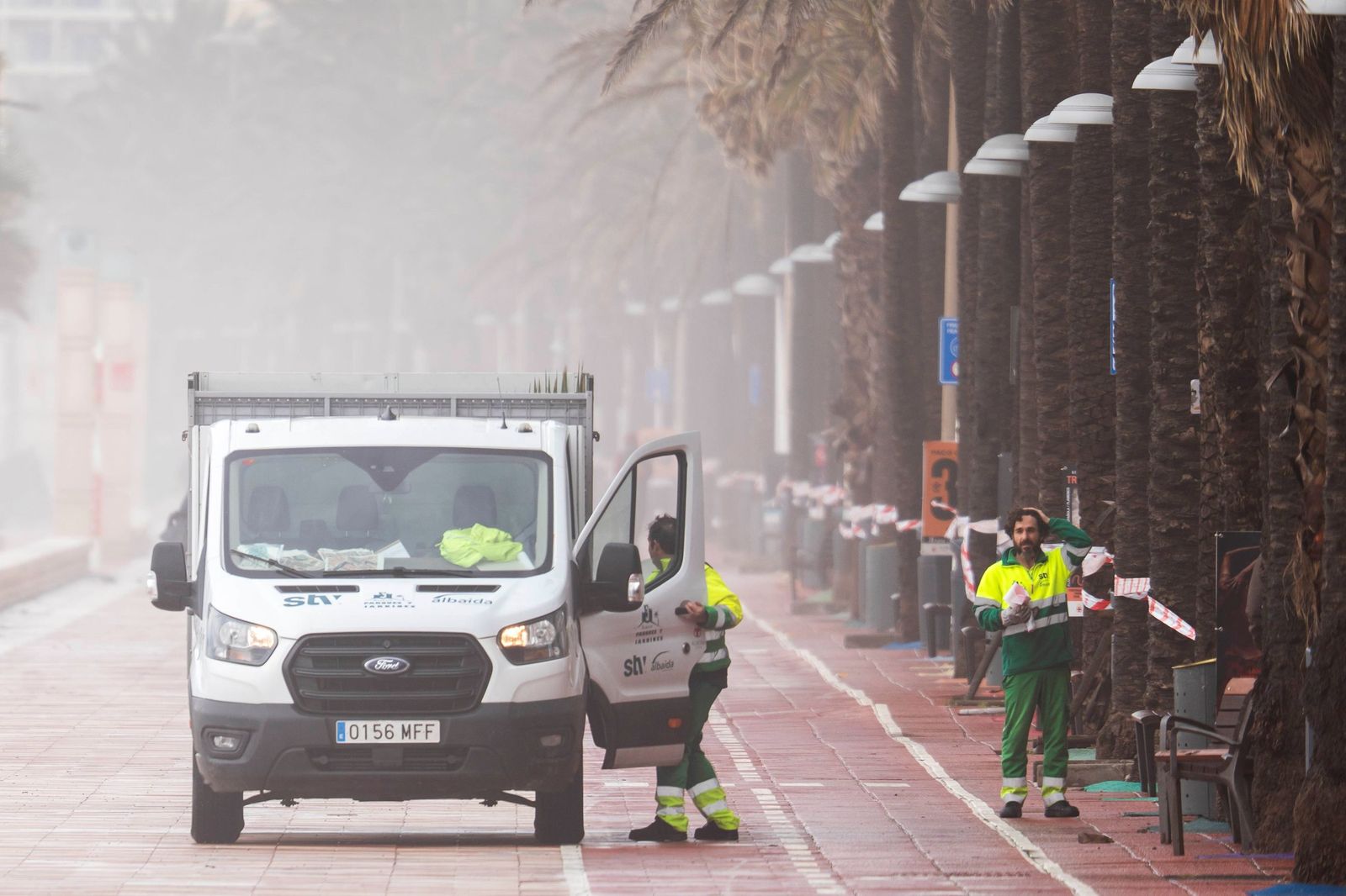 Operarios municipales trabajan en el Paseo Marítimo de Almería durante un episodio de fuerte viento y reducción de visibilidad provocado por el temporal.