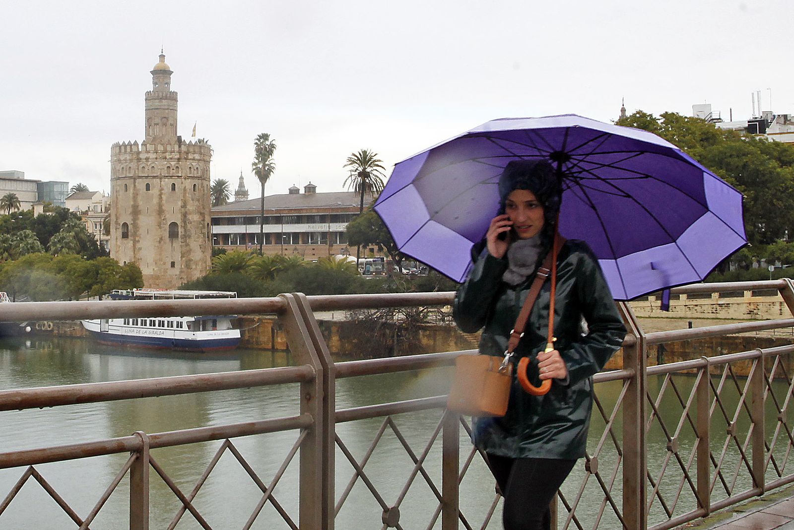 Una joven camina bajo la lluvia por el puente de San Telmo.