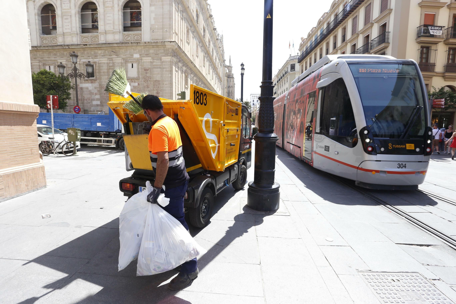 Un operario de Lipasam recoge varias bolsas con basura junto al tranvía.