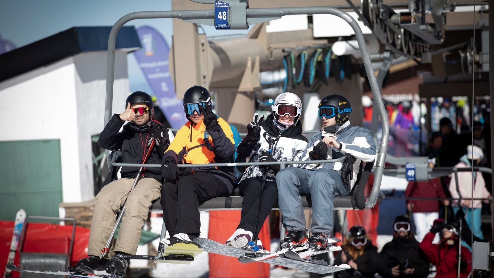 Esquiadores y snowboarders saludan desde un telesilla