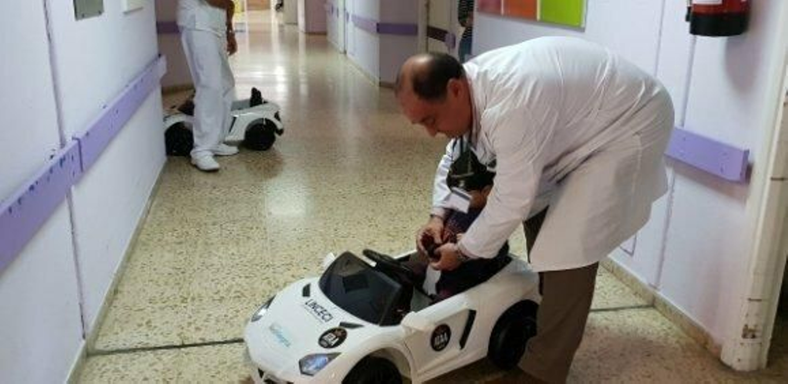 El gerente del Puerta del Mar ayuda a un menor a abrocharse el cinturón de uno de los cochecitos donados por Linceci el pasado mes de mayo.