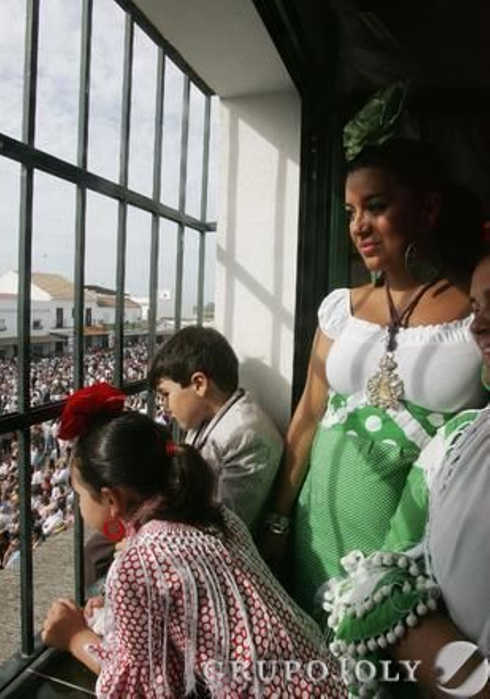 Una rociera y dos pequeños romeros contemplando el paso de la Virgen asomados a una ventana de la casa de hermandad.

Foto: Pascual