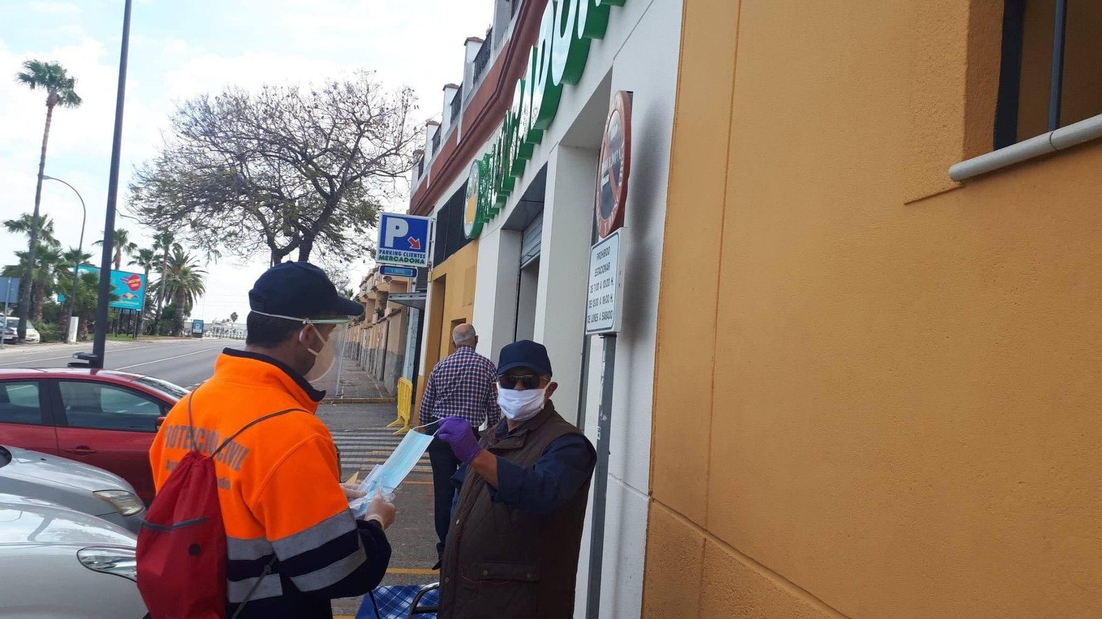 Un voluntario de Protección Civil entrega mascarillas junto a un supermercado.