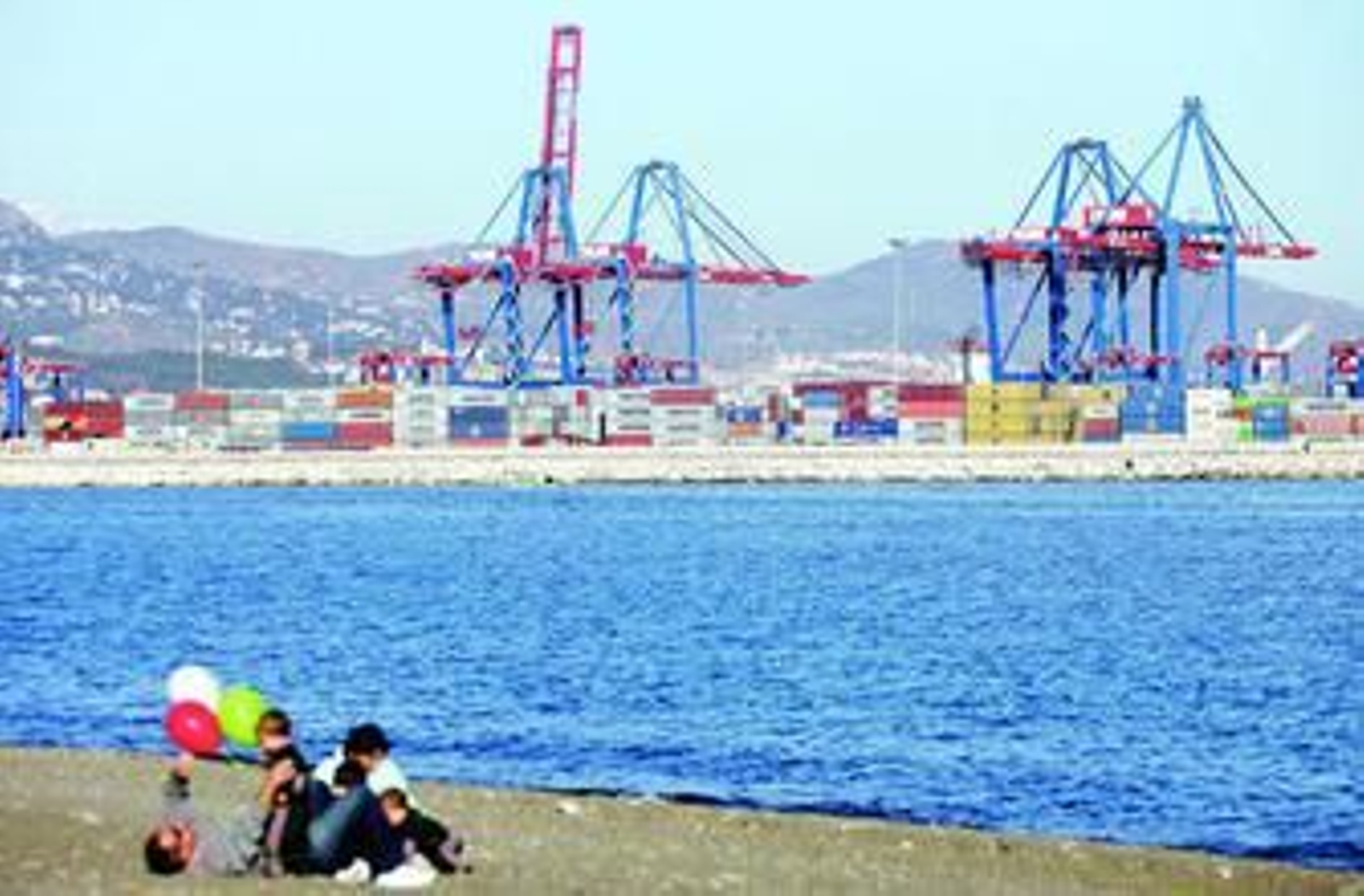 Un hombre juega con sus hijos en la playa de San Andrés con los contenedores del Puerto de fondo.