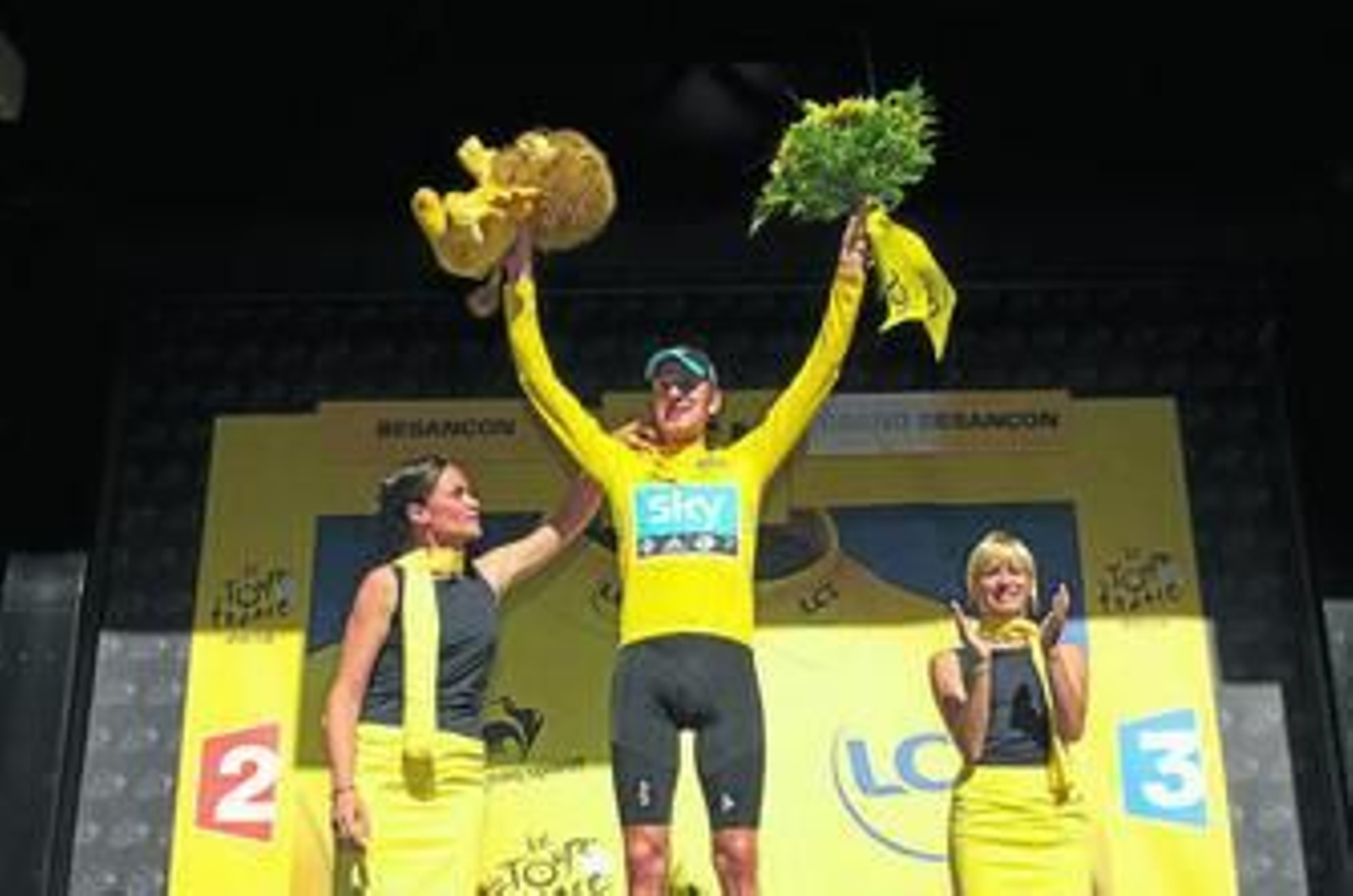 Bradley Wiggins levanta los brazos en señal de victoria en el podio de Besançon.