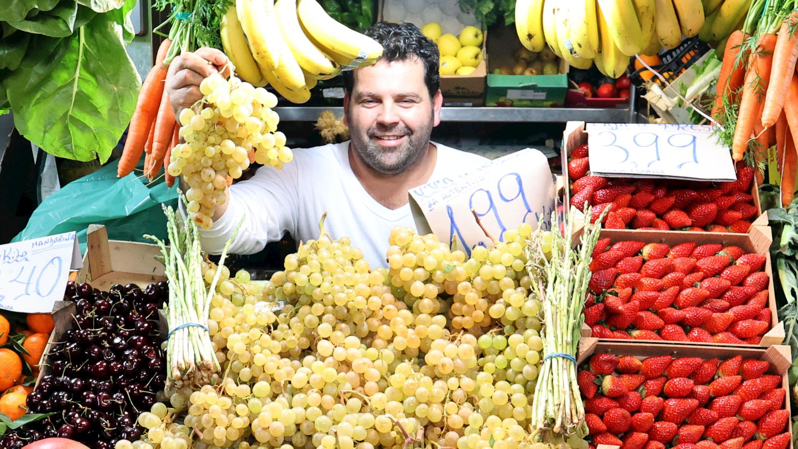 El vendedor de un puesto de frutas muestra un racimo de uvas
