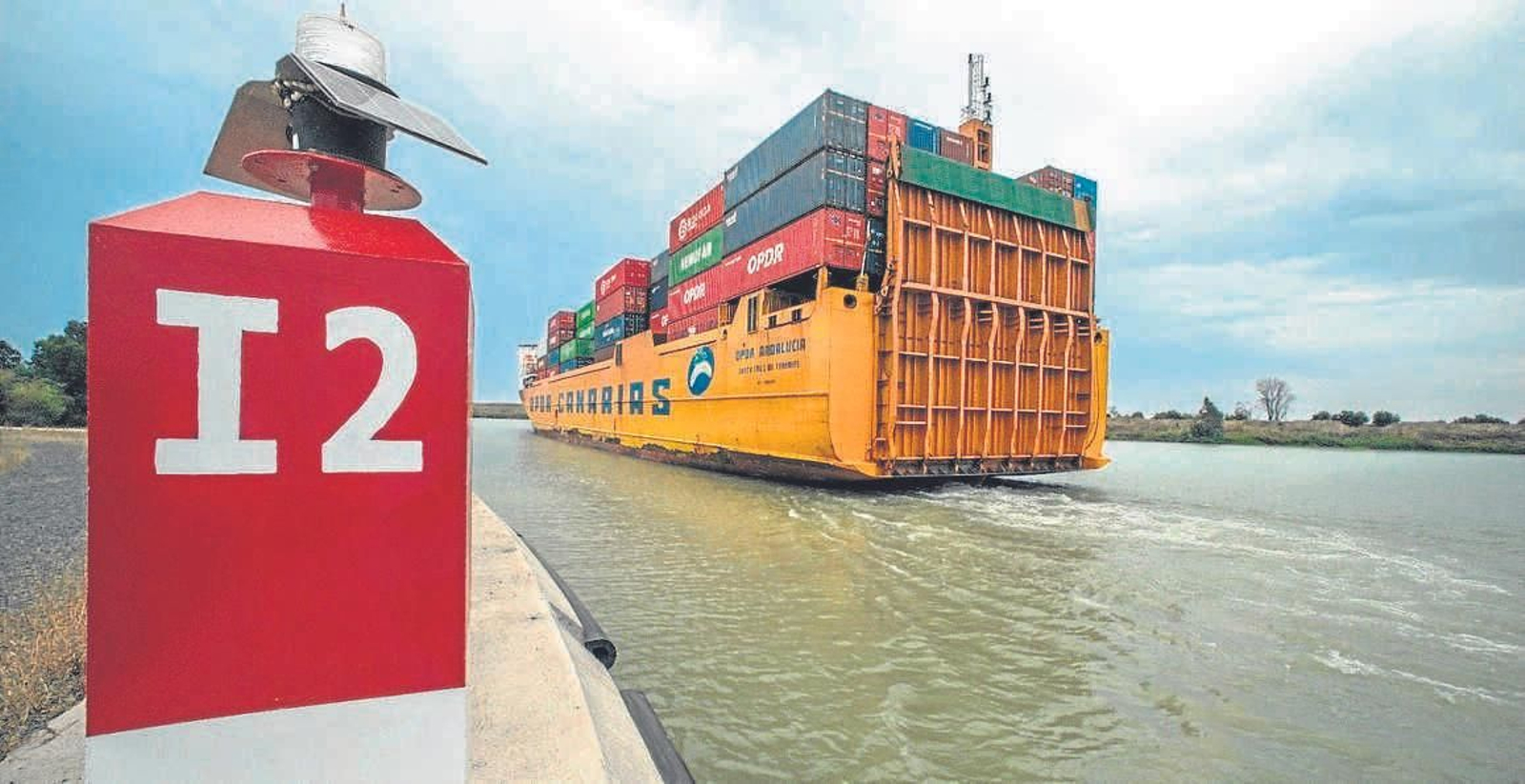 Un buque con contenedores pasa junto a una señal marítima en el Guadalquivir.