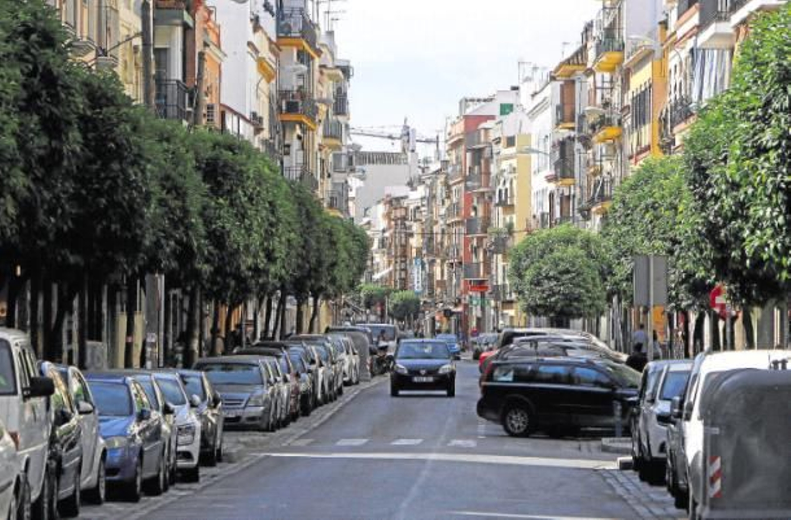 Un coche circula por la calle Feria entre dos filas de aparcamientos repletas de vehículos.