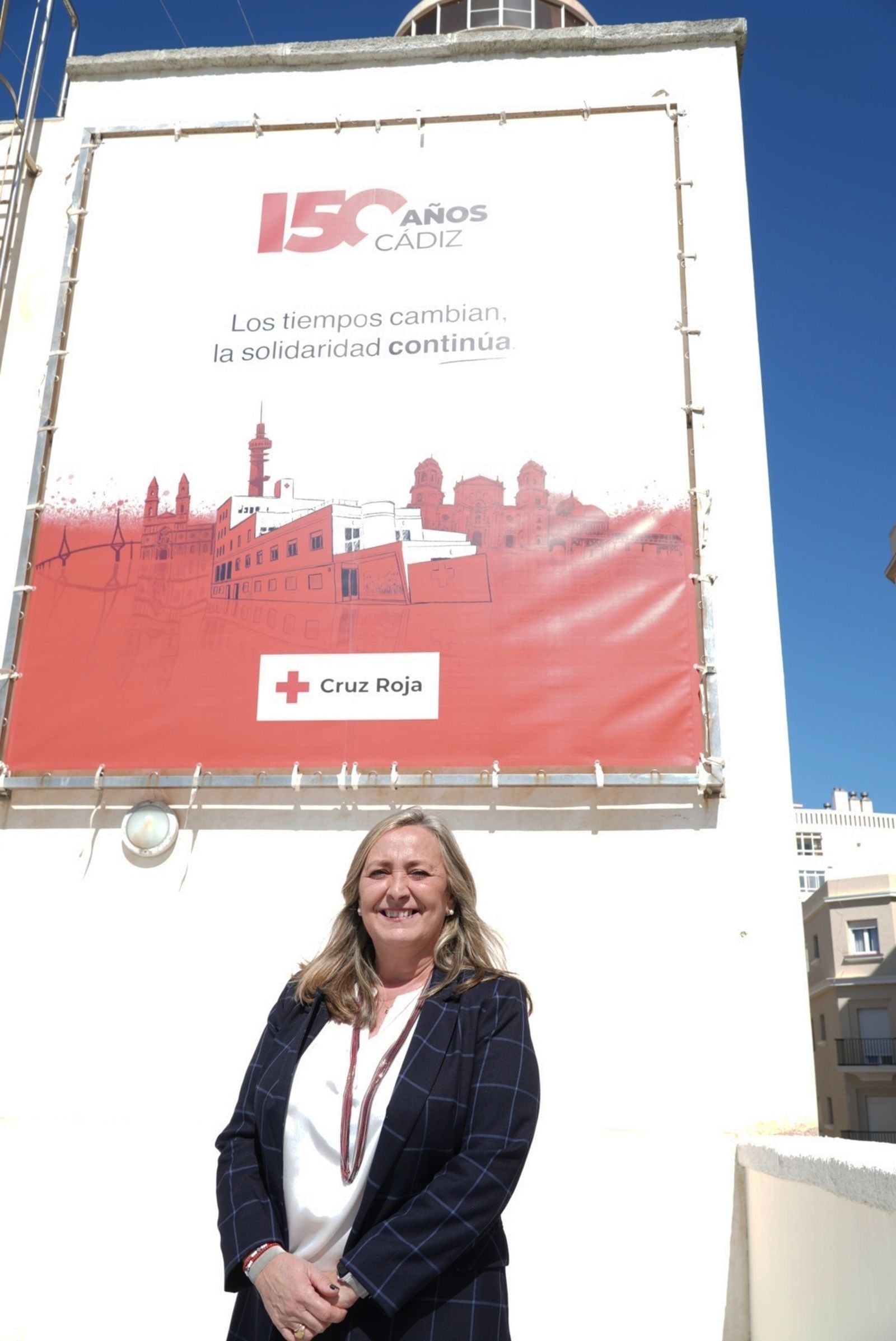 Carmen de Lara, presidenta provincial de Cruz Roja en Cádiz, ante el cartel del 150 aniversario.