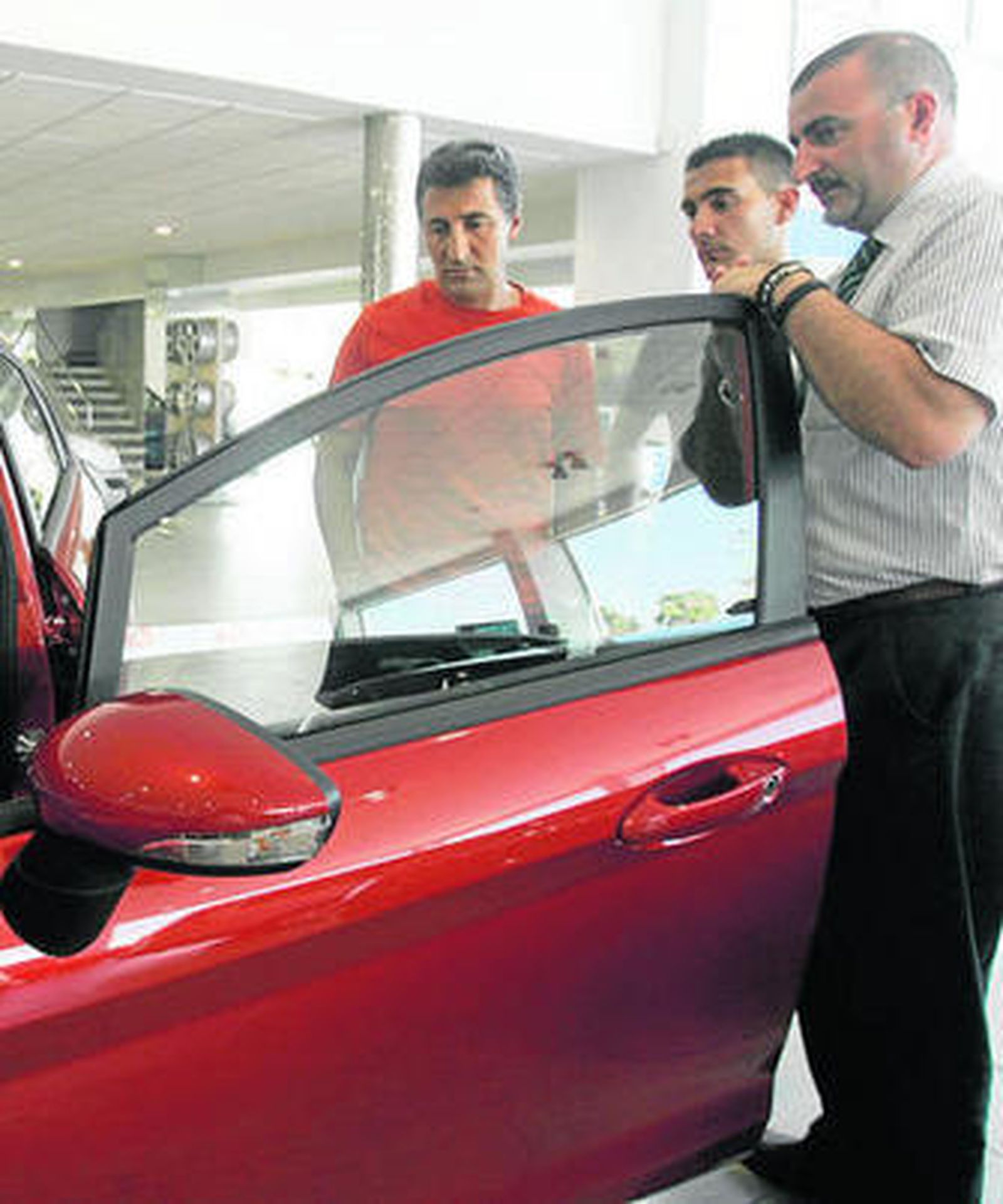 Dos personas siguen las explicaciones de un vendedor en un concesionario.