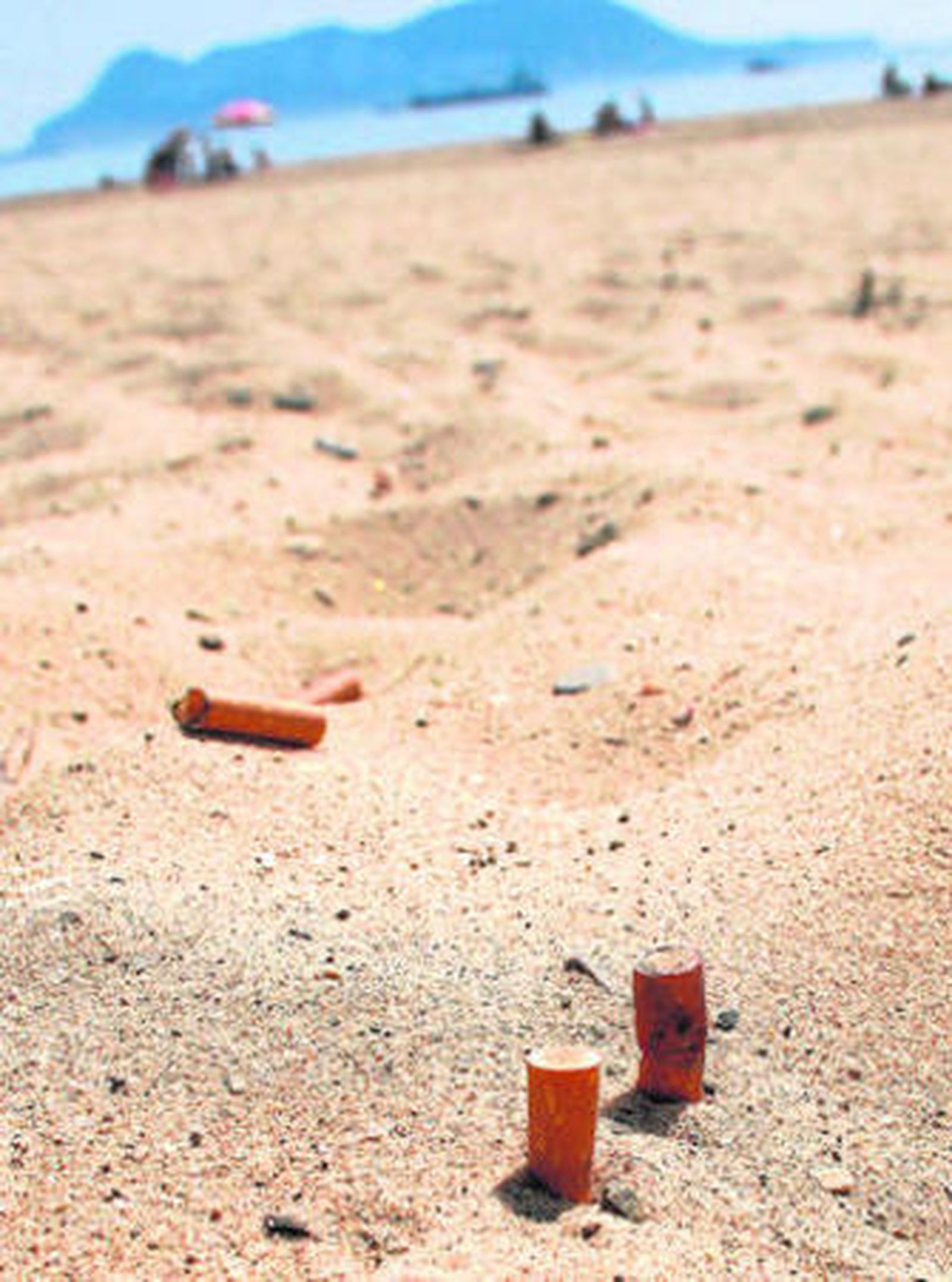 Varias colillas enterradas en la arena de una de las playas de la comarca, con el Peñón al fondo.