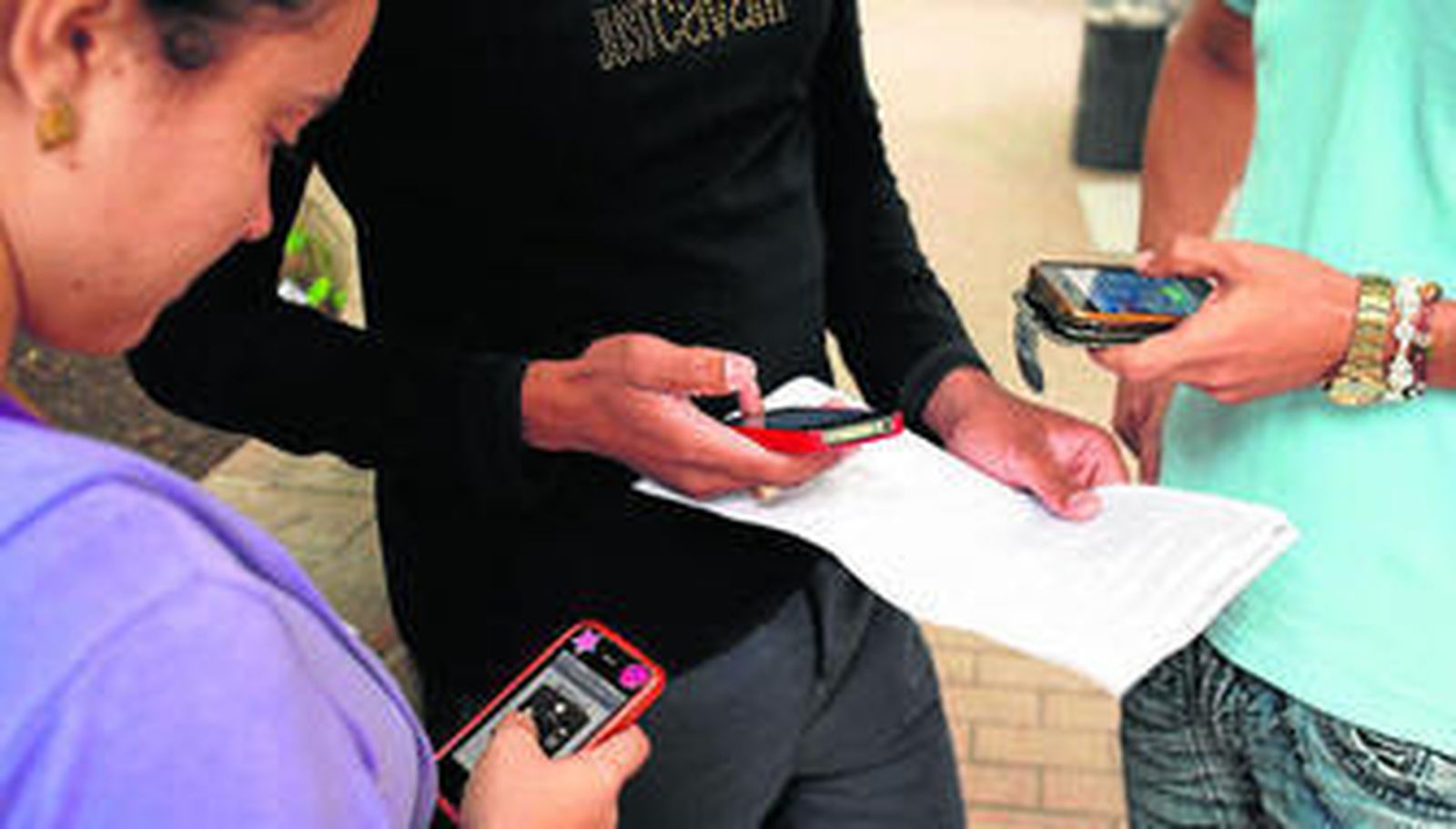 Tres jóvenes usan sus teléfonos móviles.