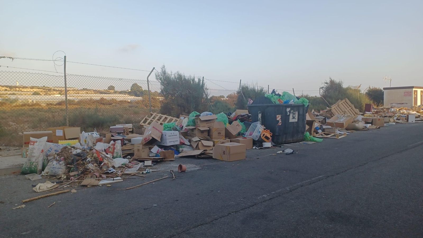 Contenedor de la basura completo en medio de la alfombra de residuos.