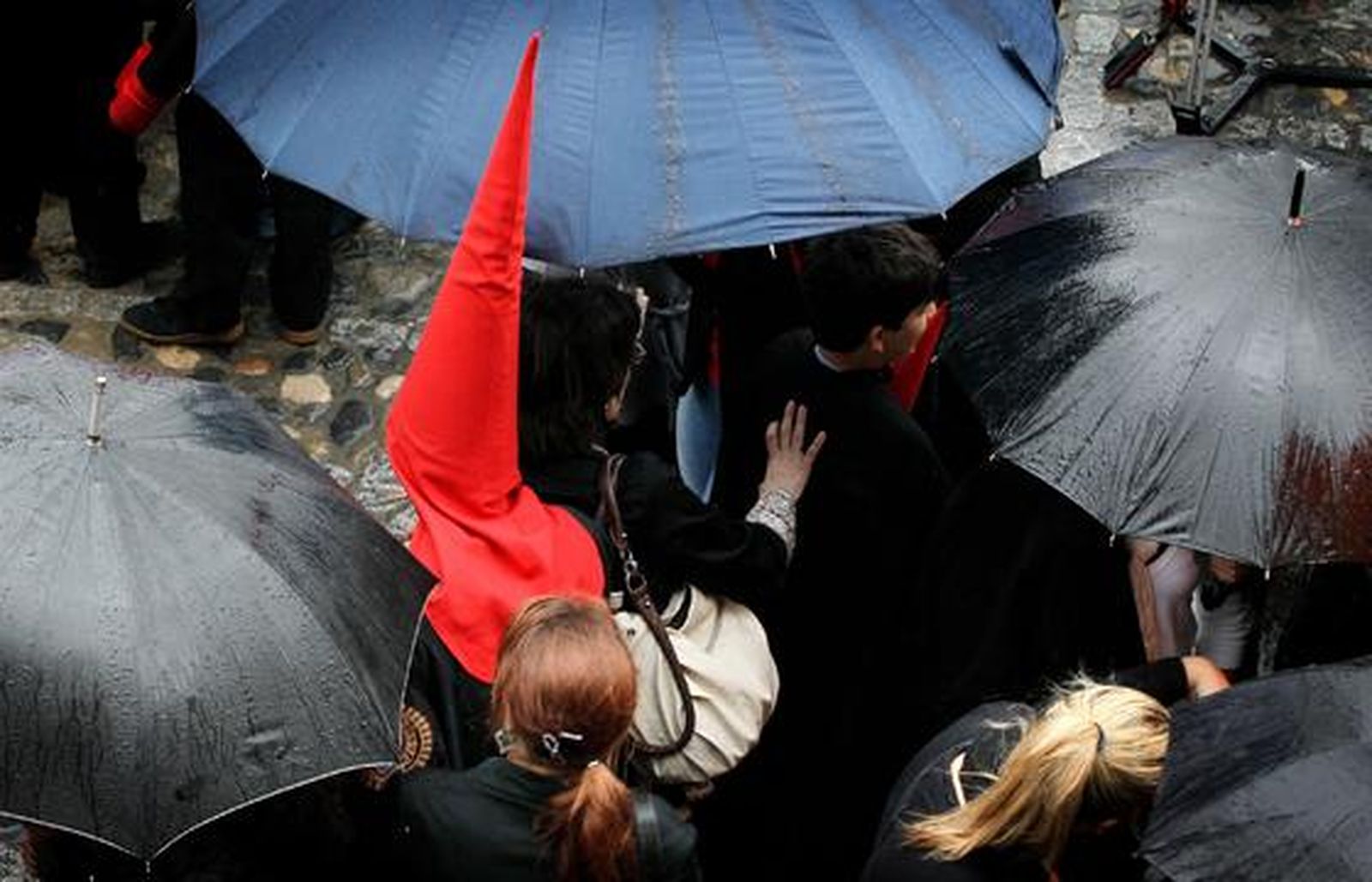 Un nazareno de la Hermandad del Desconsuelo se abre paso entre las personas que, con paraguas, aún esperaban que Los Judíos se hicieran a la calle.

Foto: Miguel Ángel González