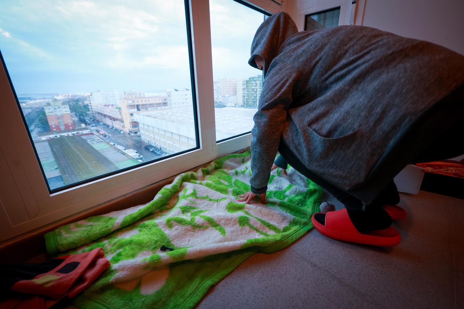 Una vecina trata de que el agua no siga entrando por la ventana de su casa con toallas y mantas.