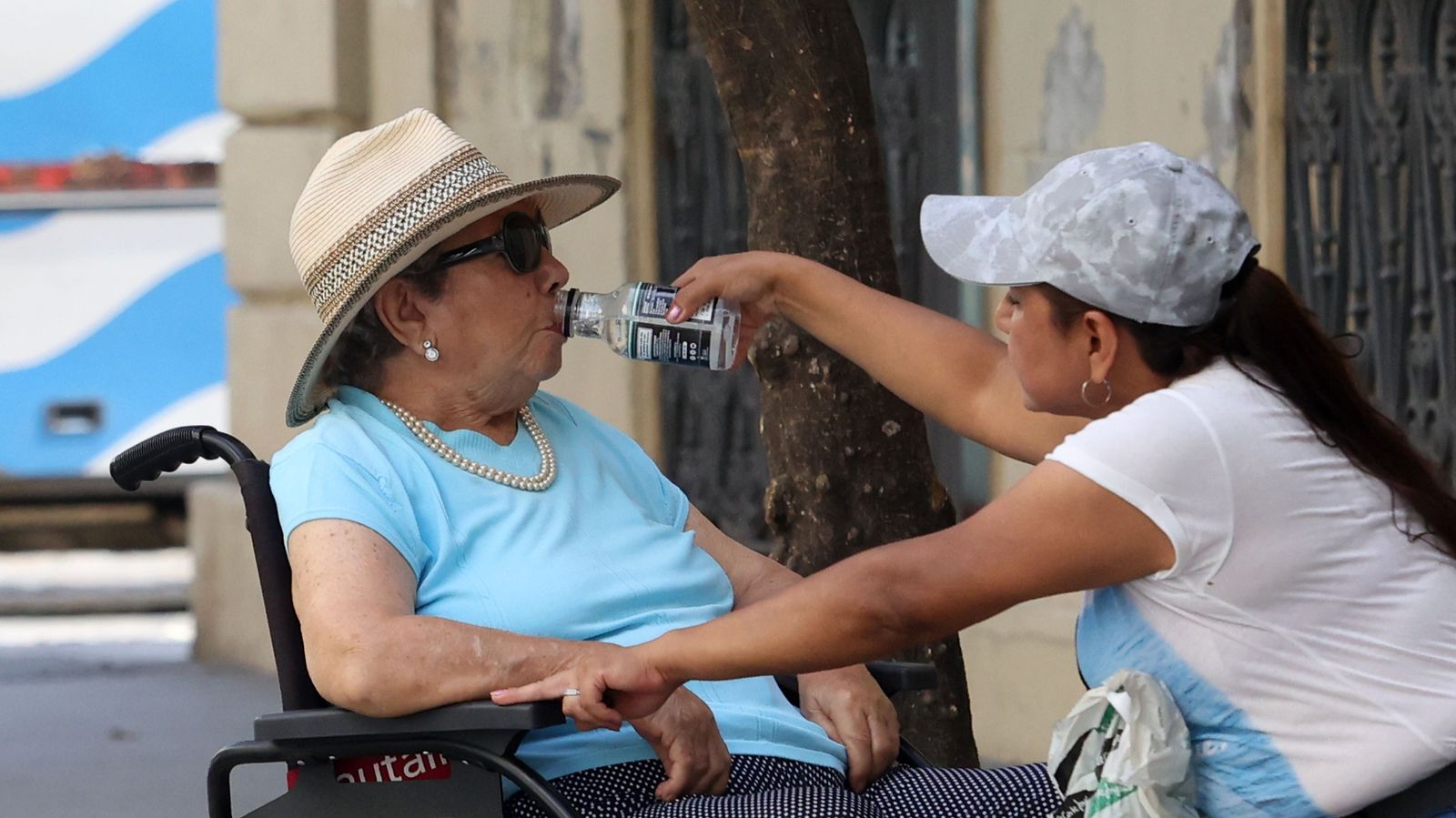 Una mujer refresca a otra con una botella de agua mientras pasean en una calle del centro de Jerez