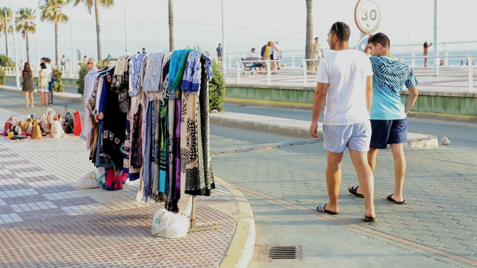 Dos chicos se bajan de la acera ante la incomodidad de esquivar percheros y mantas.