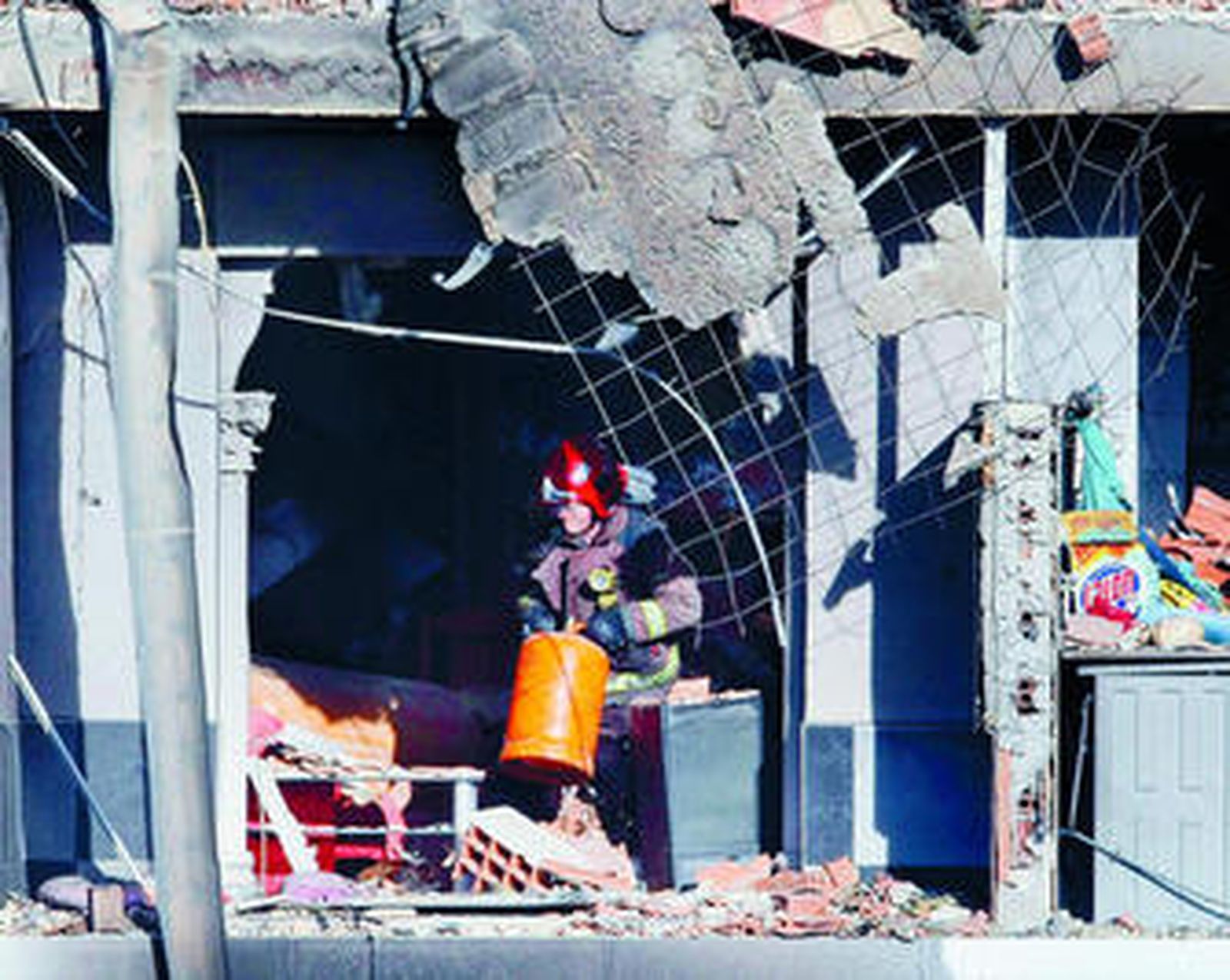 Un bombero mueve una bombona de gas en el edificio destrozado tras la explosión.