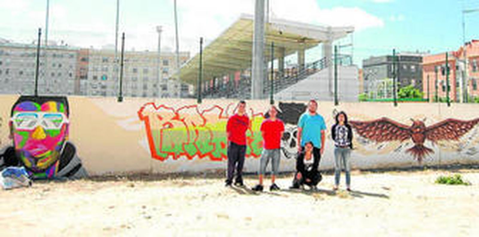 Algunos de los jóvenes artistas, ante el muro del campo de fútbol de La Bazán, con la delegada de Juventud.