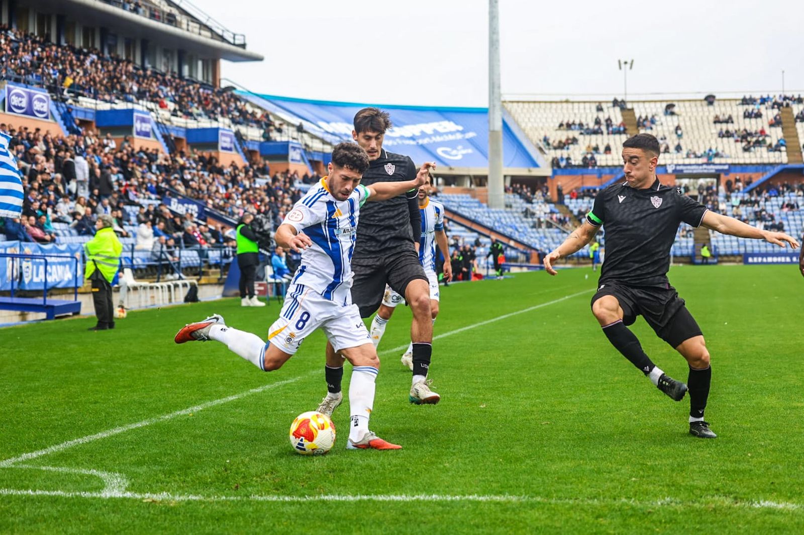 Pepe Mena pone un centro encimado por dos jugadores del Almería B.