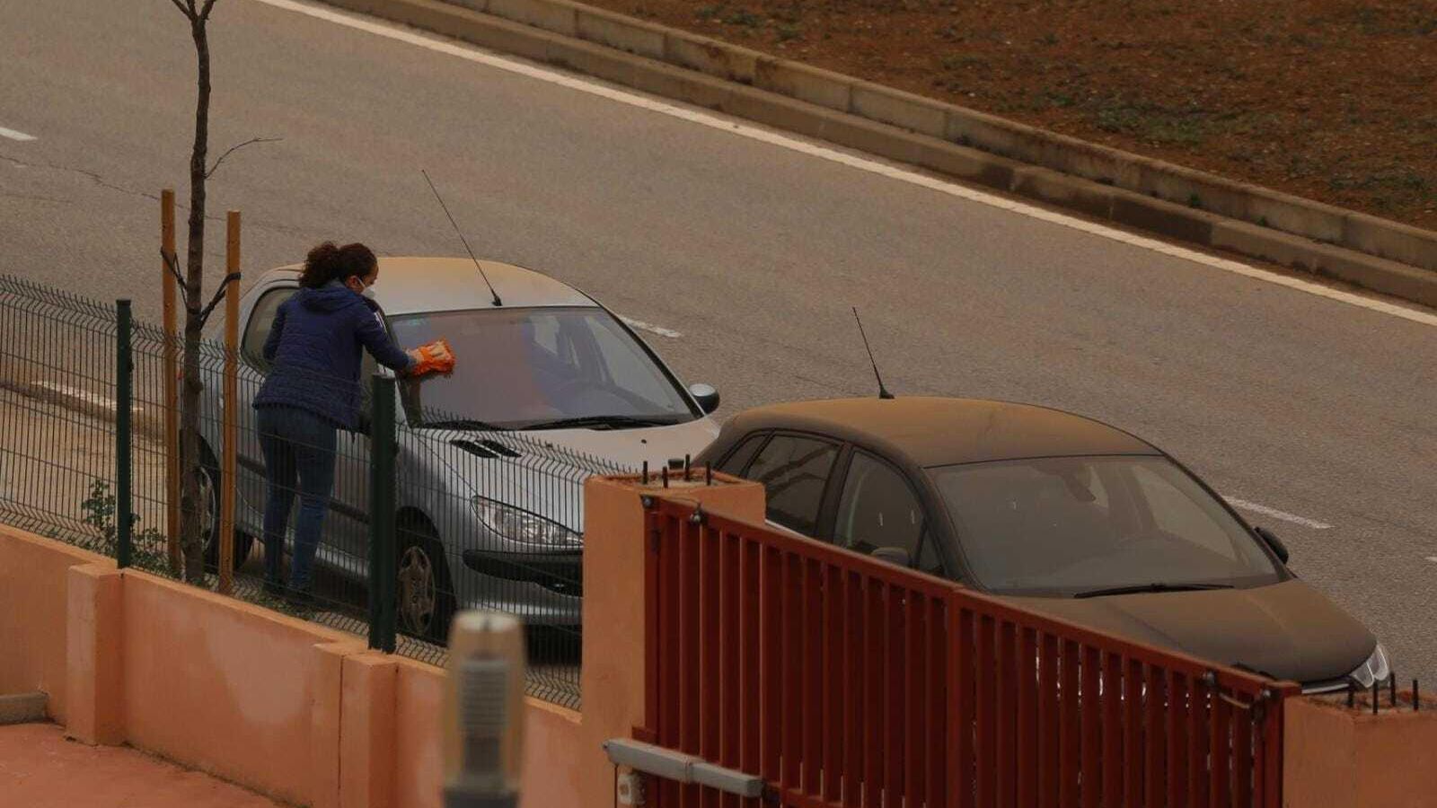 Una mujer limpia el polvo de la calima de su coche.
