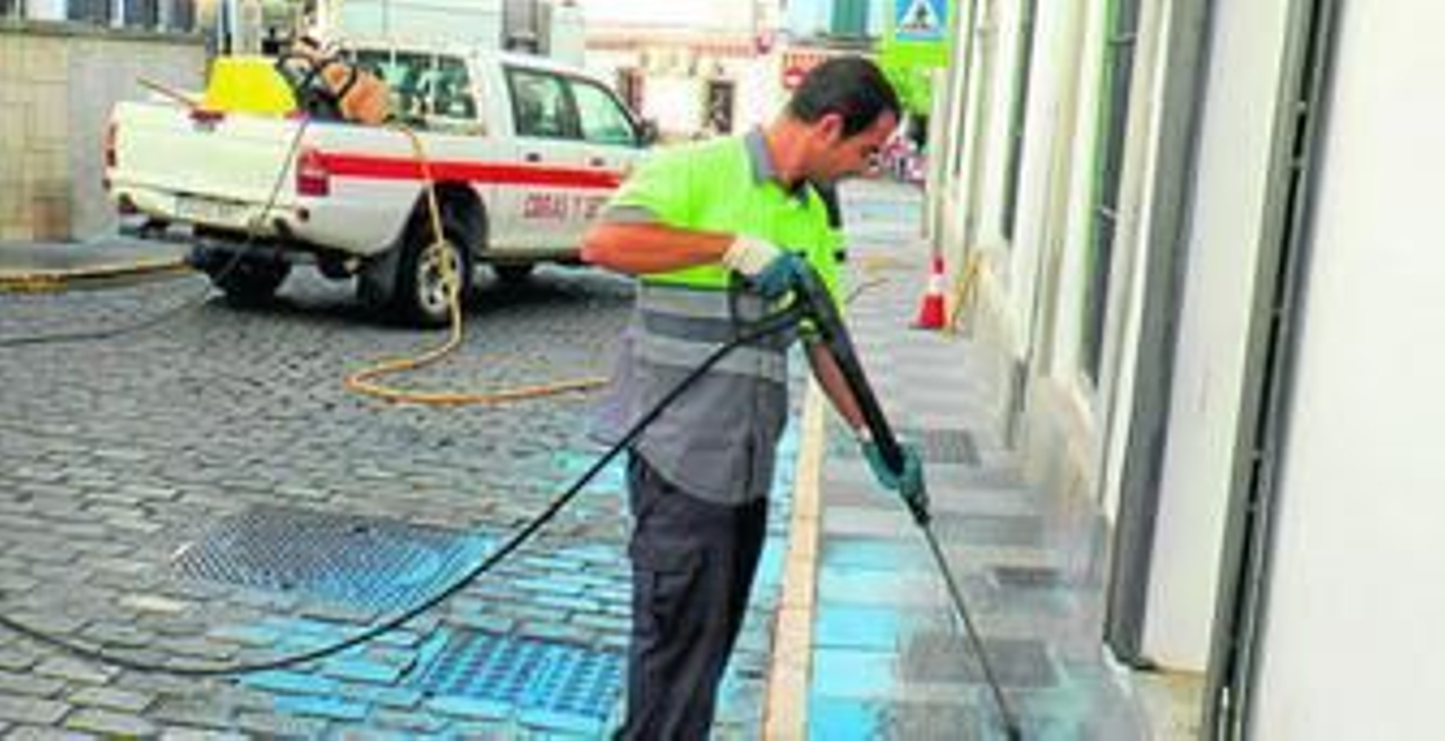 Un operario limpia con agua a presión una de las aceras de la calle Málaga.