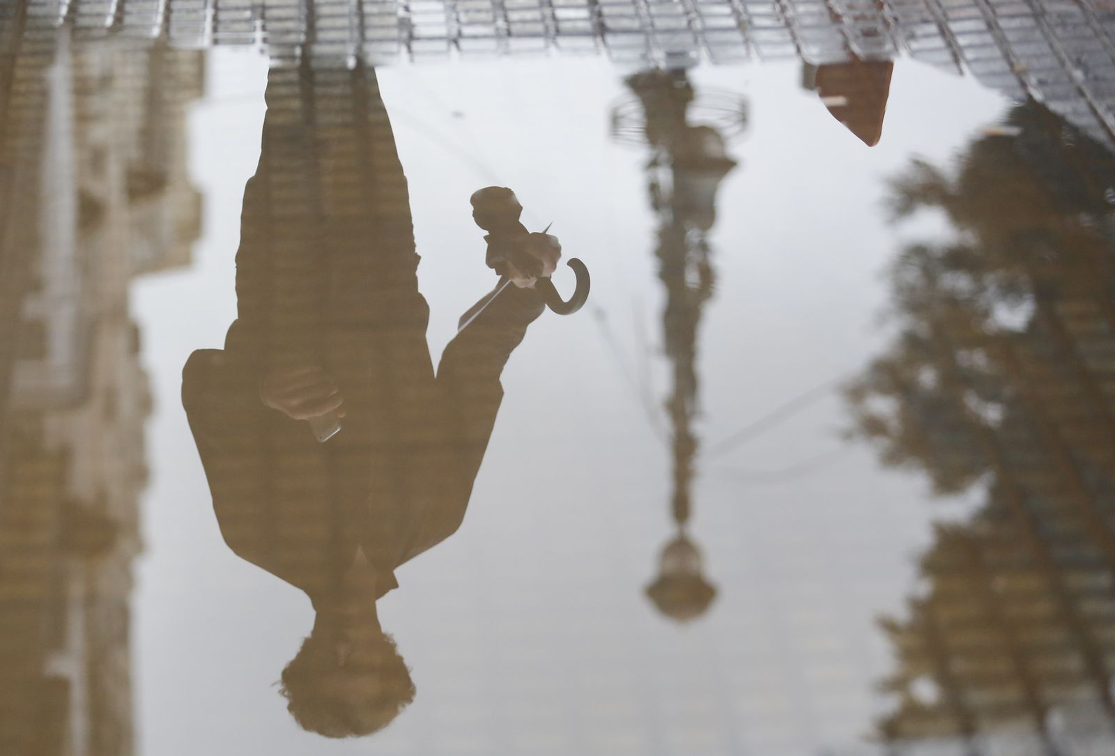 Imagen de una persona reflejada en un charco en una calle de Málaga.