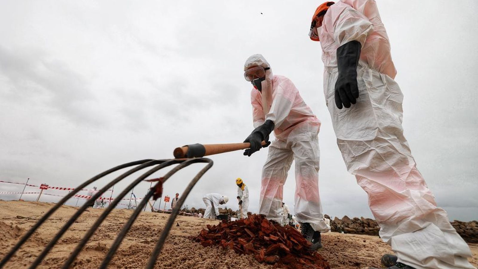Dos trabajadores equipados con trajes de protección, retirando el supuesto fueloil.