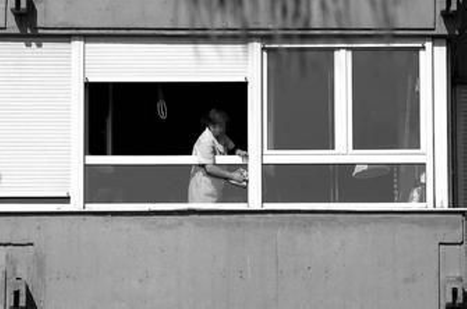 Una trabajadora del servicio doméstico, de uniforme, limpia las ventanas de un piso.