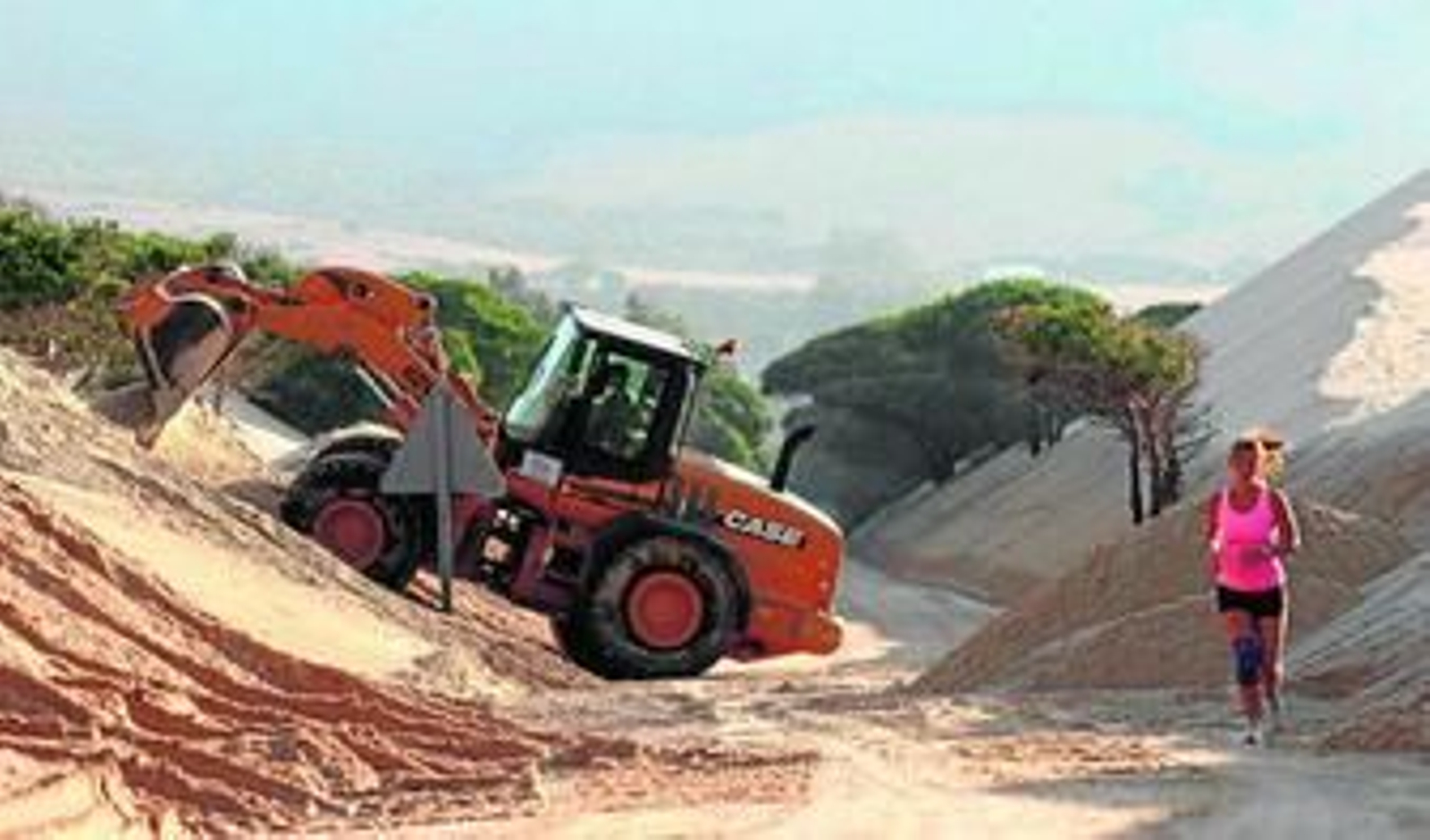 Una joven practica deporte a la altura de una excavadora que recoge arena ayer en las cercanías de la playa de Valdevaqueros, en Tarifa.