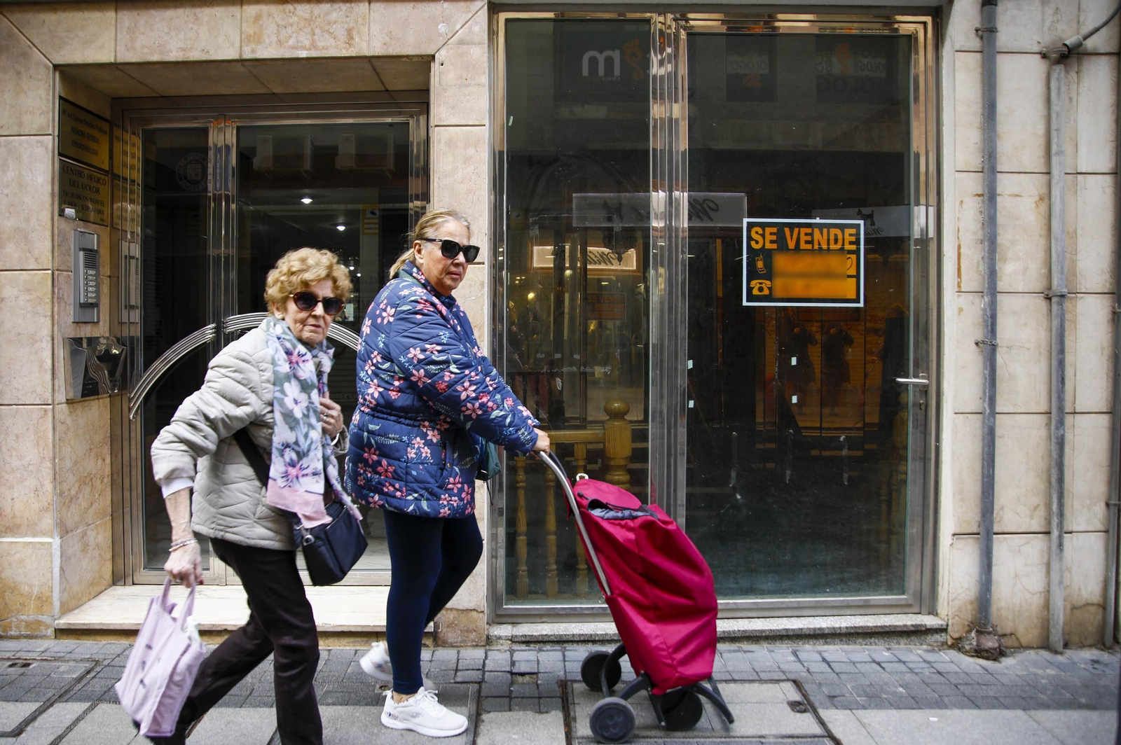 Dos personas pasan junto a un cartel que indica la venta de una propiedad en Almería capital.