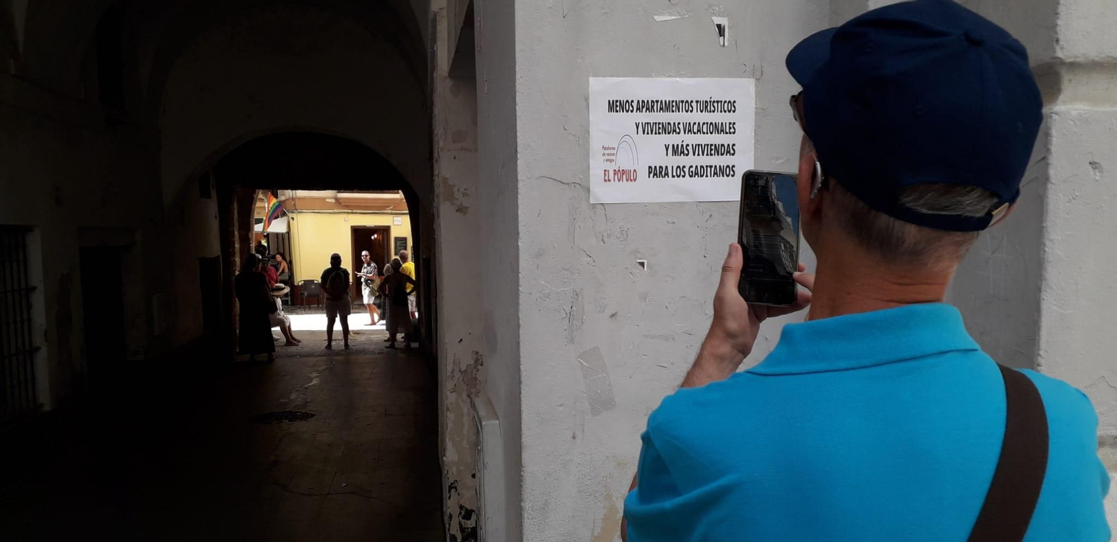 Un hombre fotografía un cartel contra la turistificación a la entrada del Arco de El Pópulo.