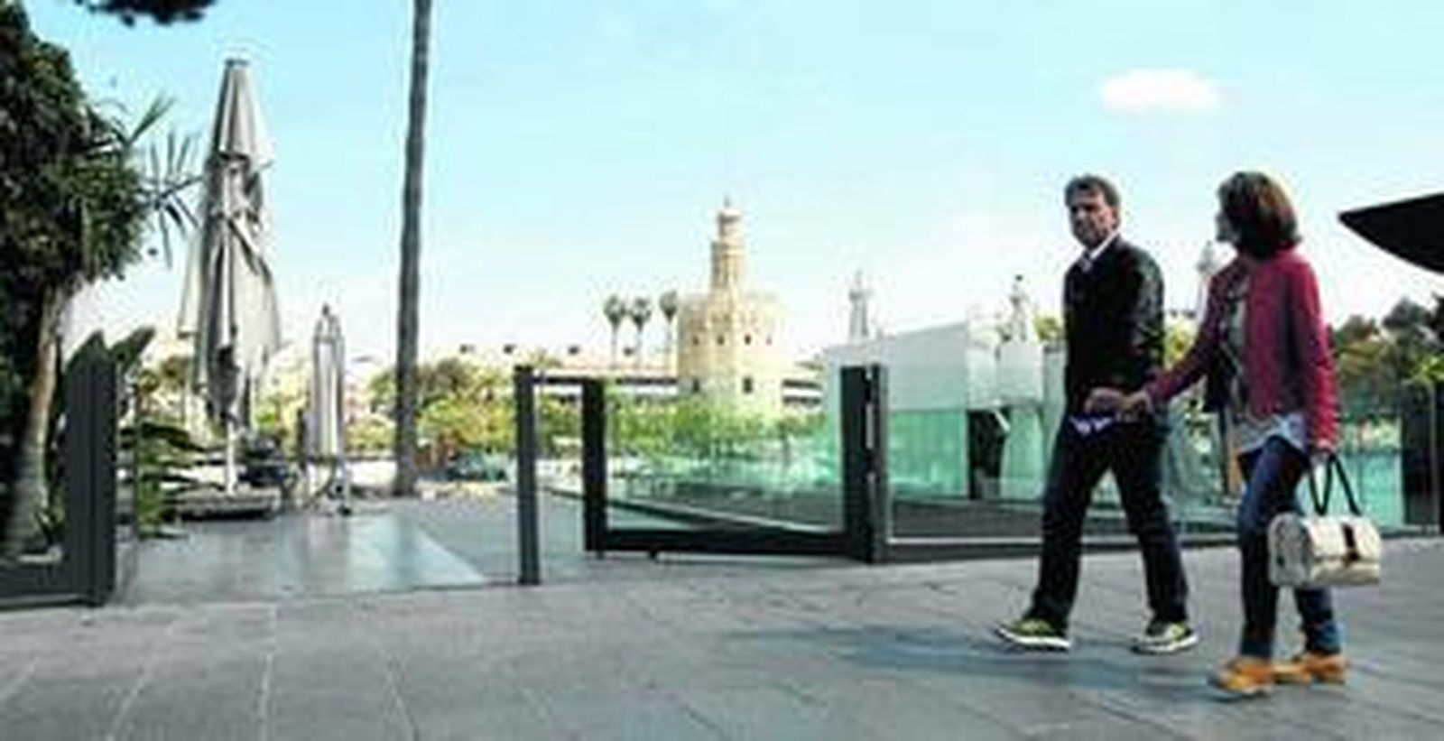 Una pareja camina junto a la valla de cristal que impide el acceso al río, en la calle Betis.