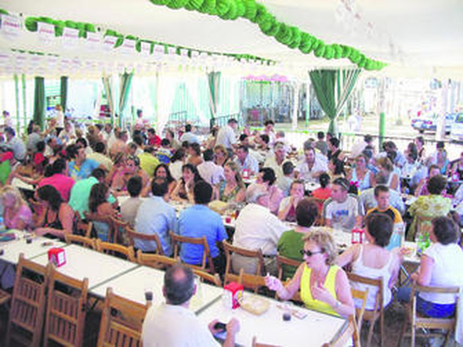 Numerosas personas disfrutan de un almuerzo ferial en la caseta bética.